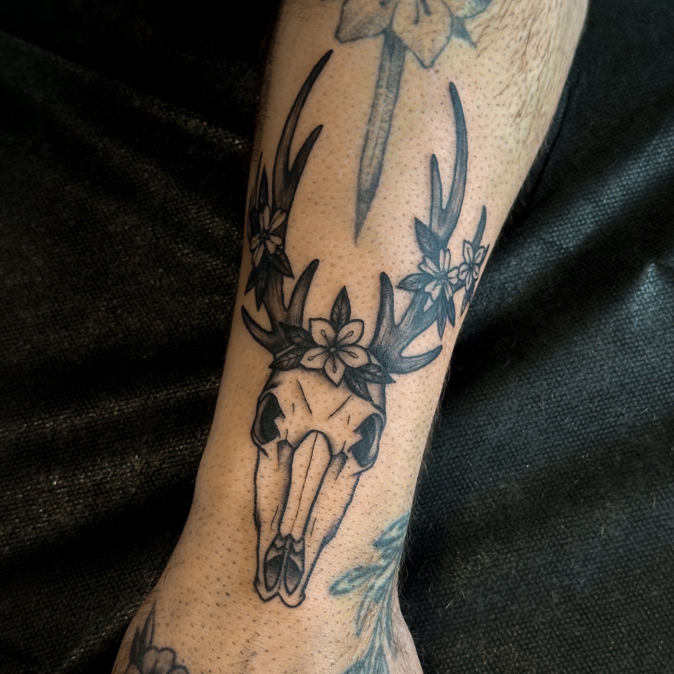Deer skull with flowers black and grey tattoo on the forearm by Victoria