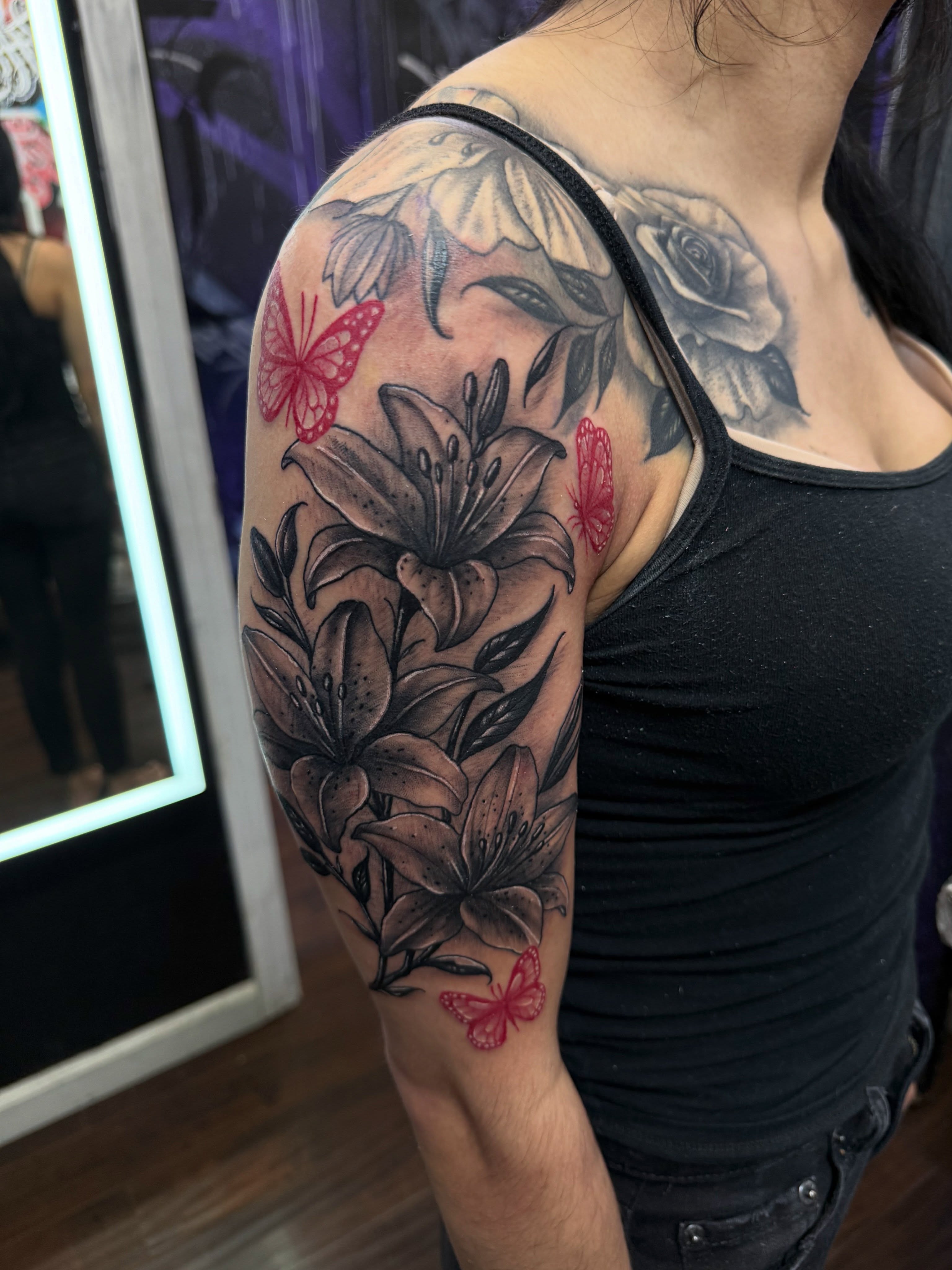 Lilies and butterflies realism tattoo on the upper arm by @samg_tat2s, San Diego, California