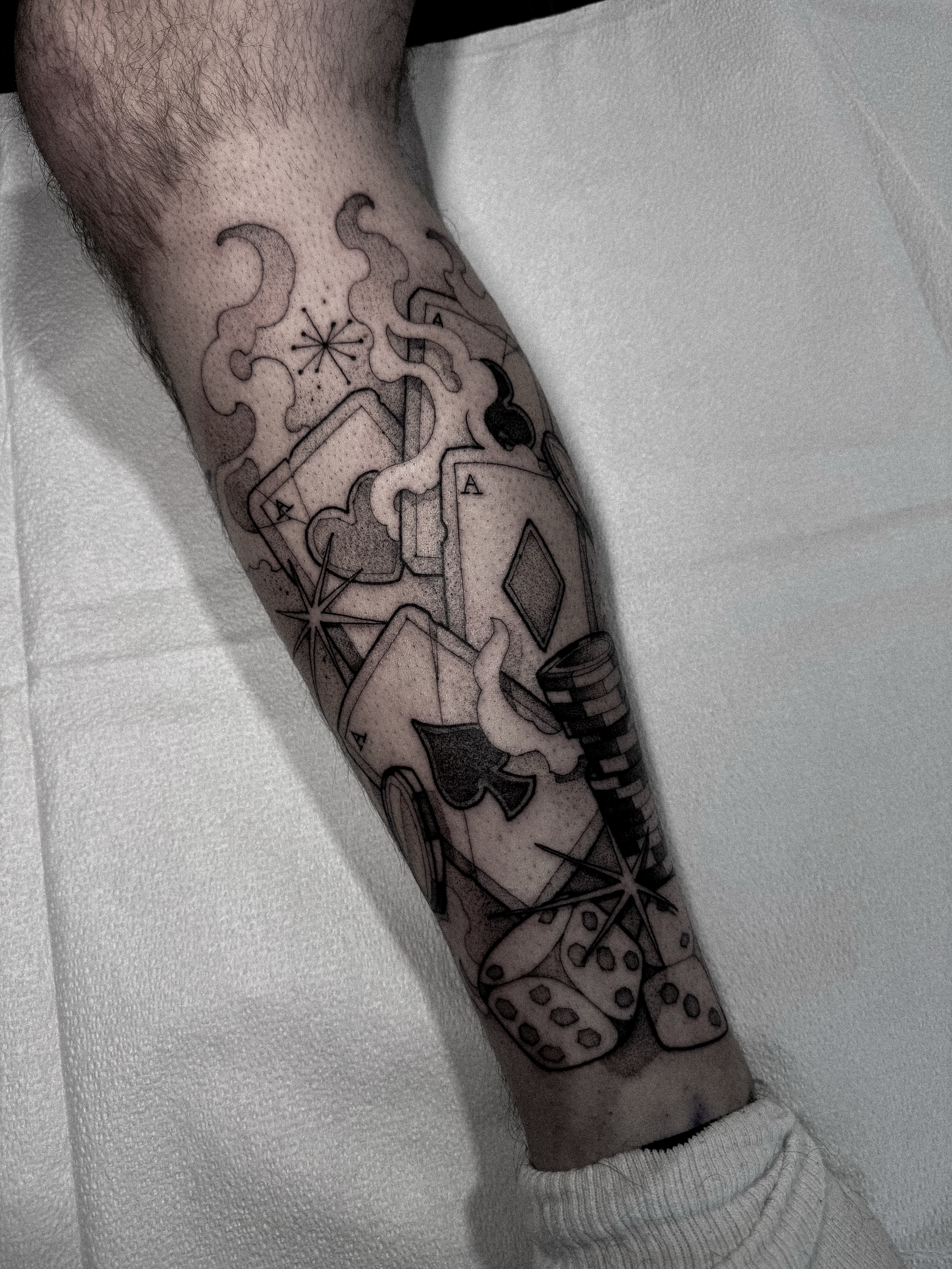 Playing cards and dice black and grey tattoo on the forearm by Dane Bezeau