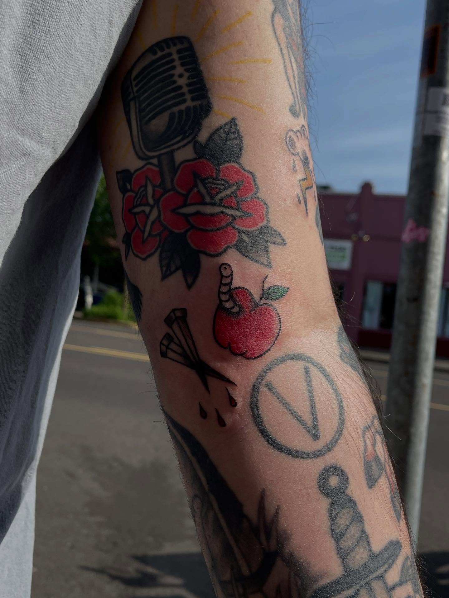 Microphone, roses, apple, peace symbol American traditional tattoo on the forearm by J❄️, Portland, Oregon