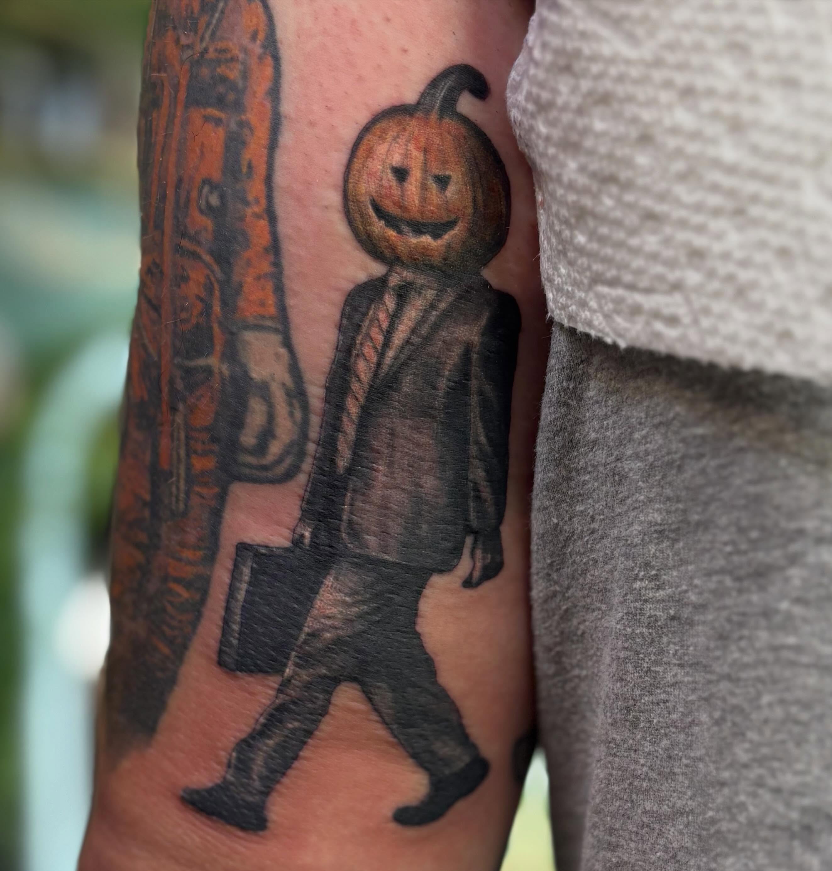 Pumpkin-headed figure black and grey tattoo on the forearm by Olivia Buch