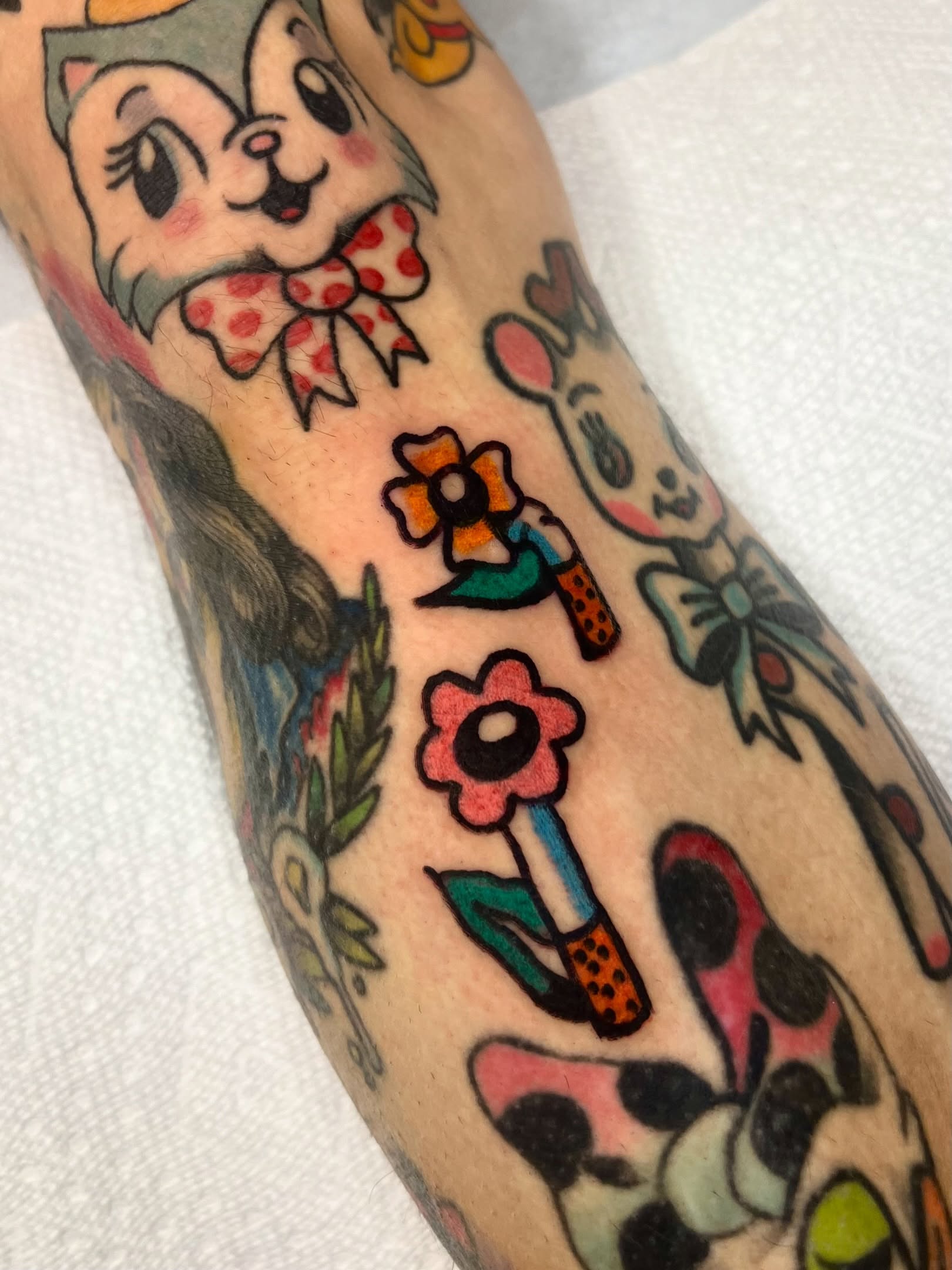 Cartoon characters and flowers American traditional tattoo on the forearm by Sierra Mack