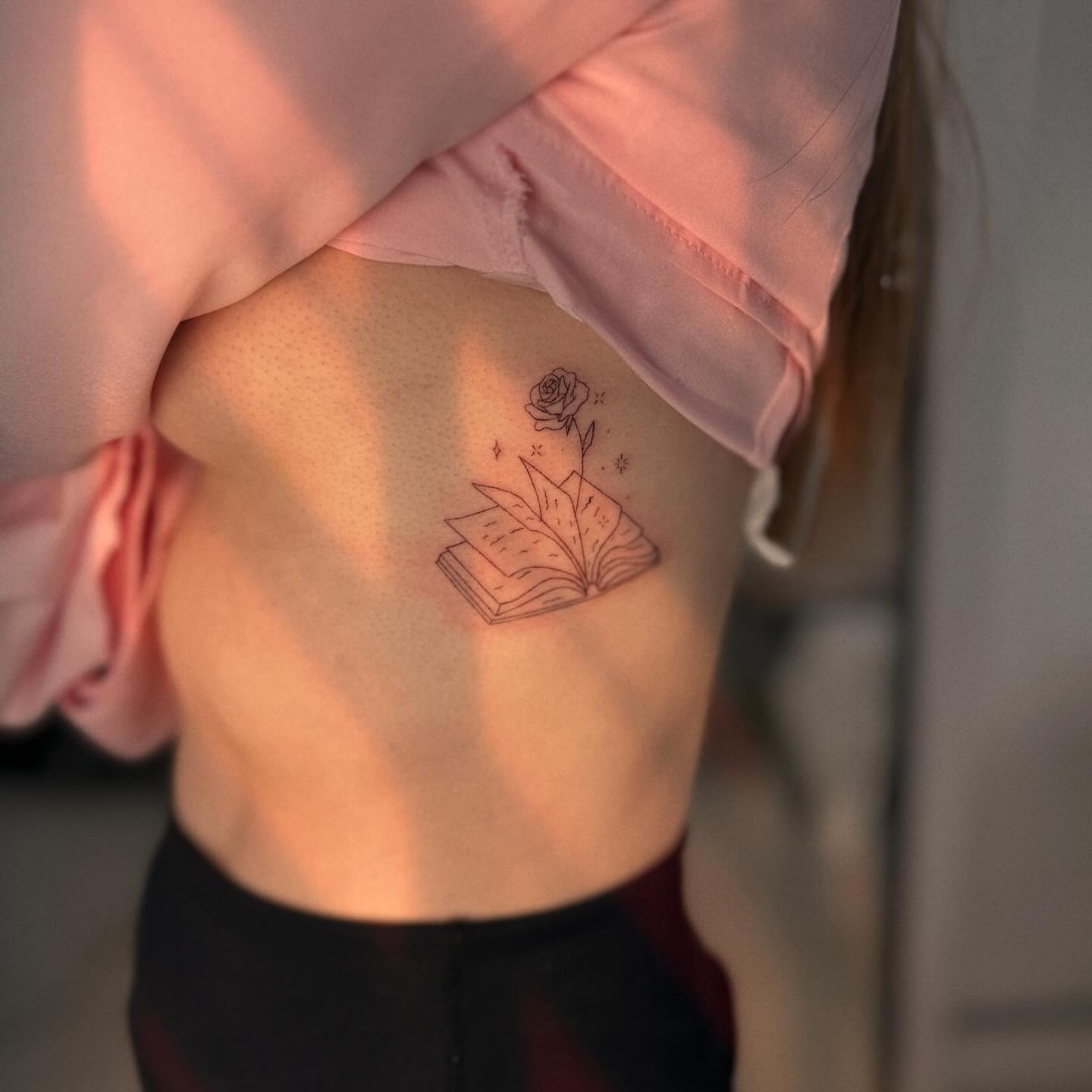 Book and rose fine line tattoo on the ribs by Ellie