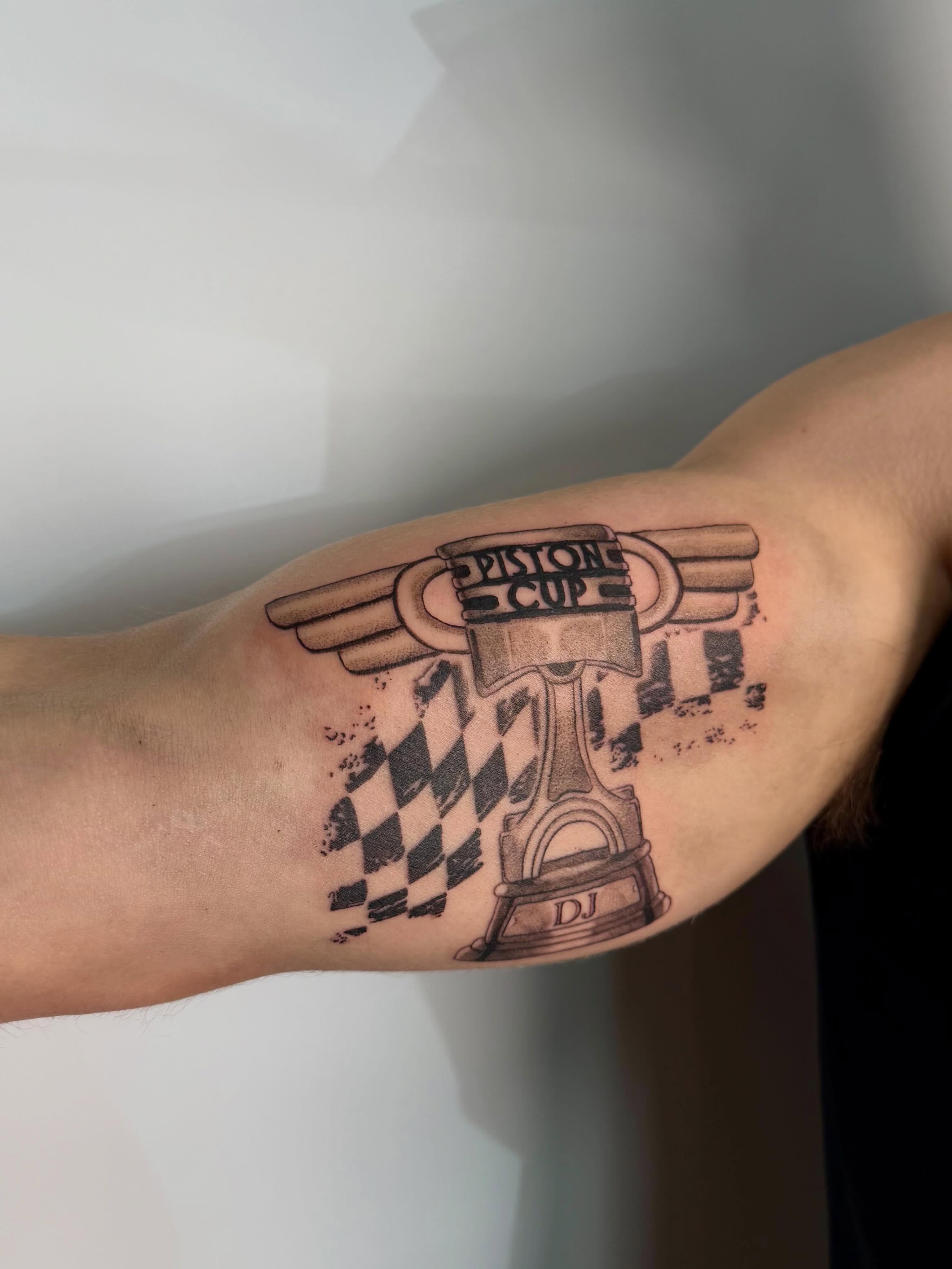 Piston cup trophy black and grey tattoo on the forearm by Bailee