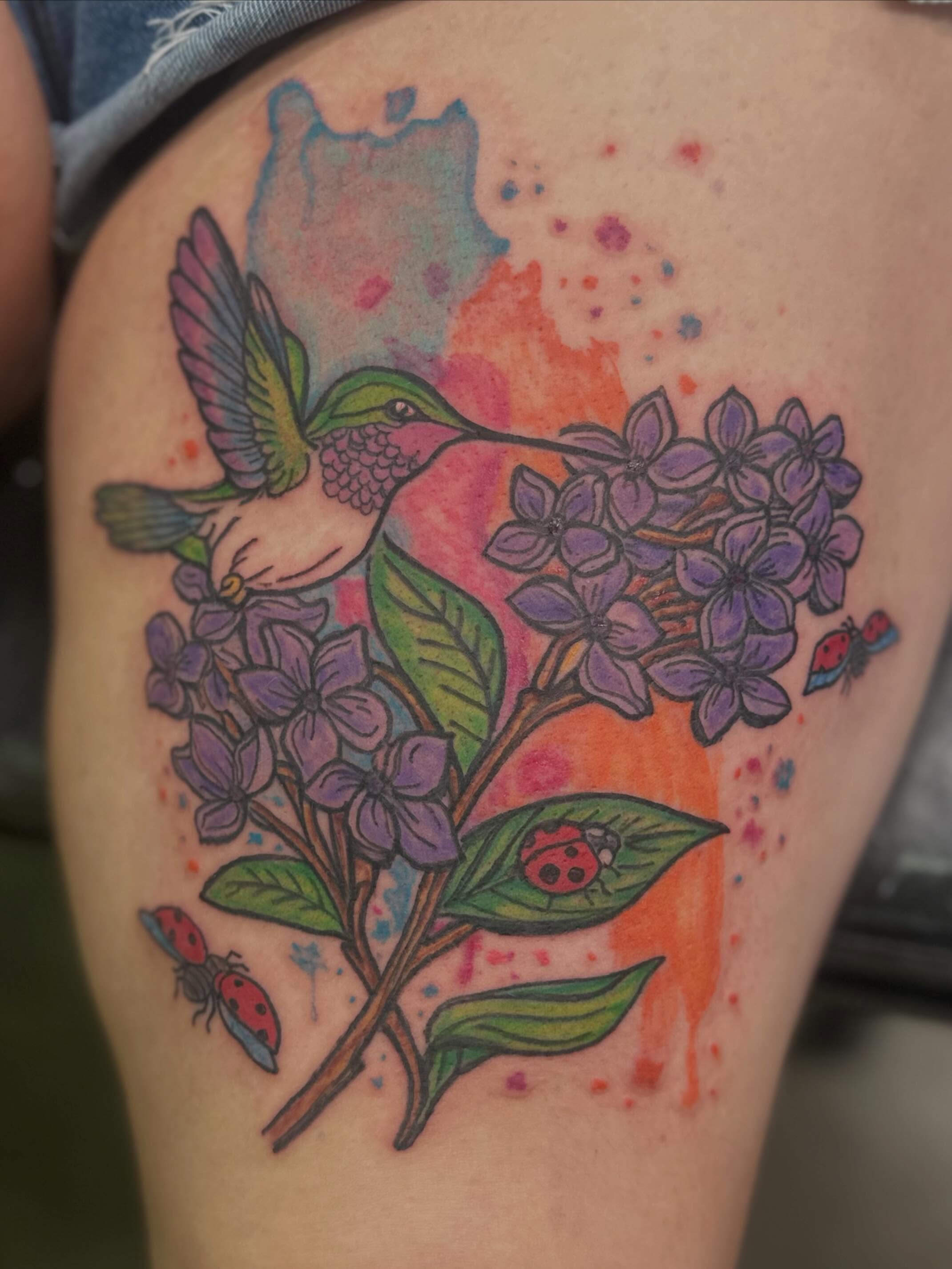 Hummingbird and lilac watercolor tattoo on the thigh by Zen Forbes
