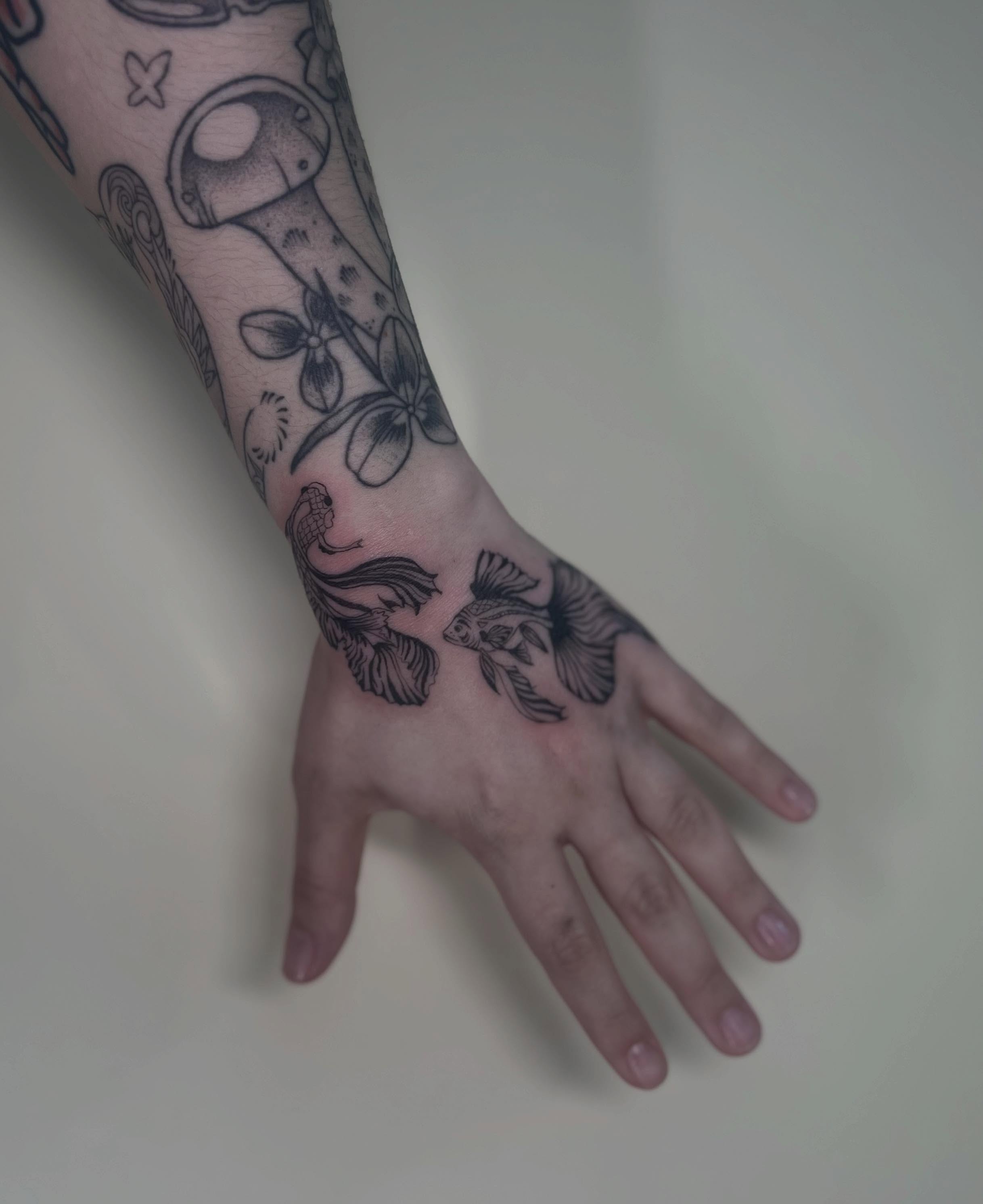 Fish and flowers black and grey tattoo on the hand by Alex