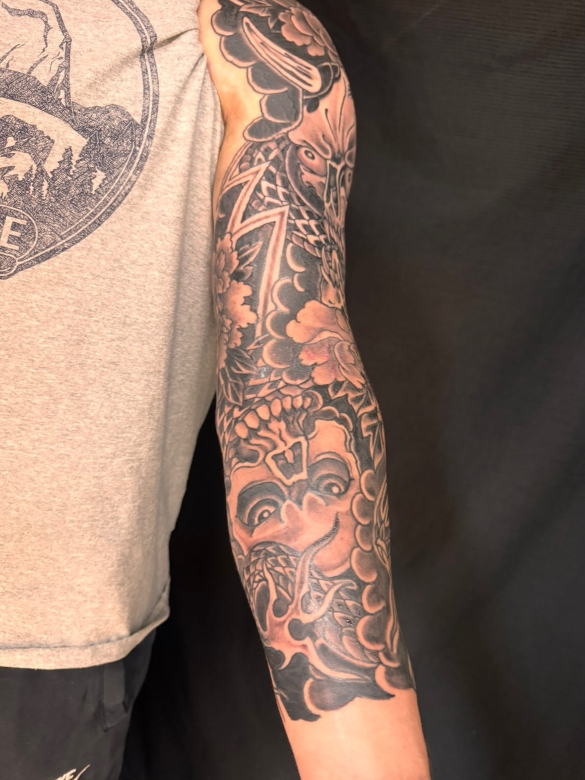 Mask and floral black and grey tattoo on the forearm by Brian Hutflies