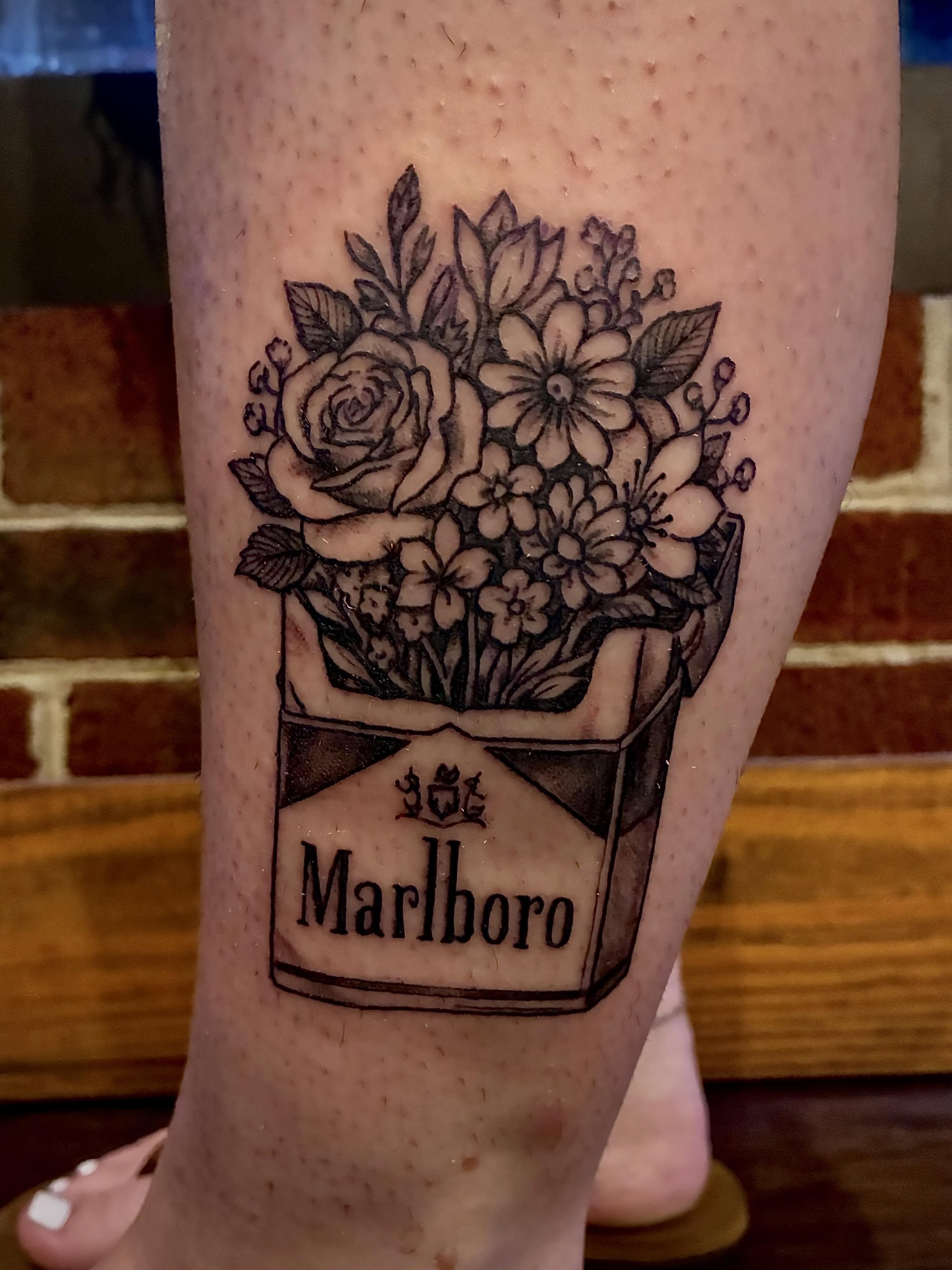 Flowers in a cigarette box black and grey tattoo on the leg by Chris Hornsby