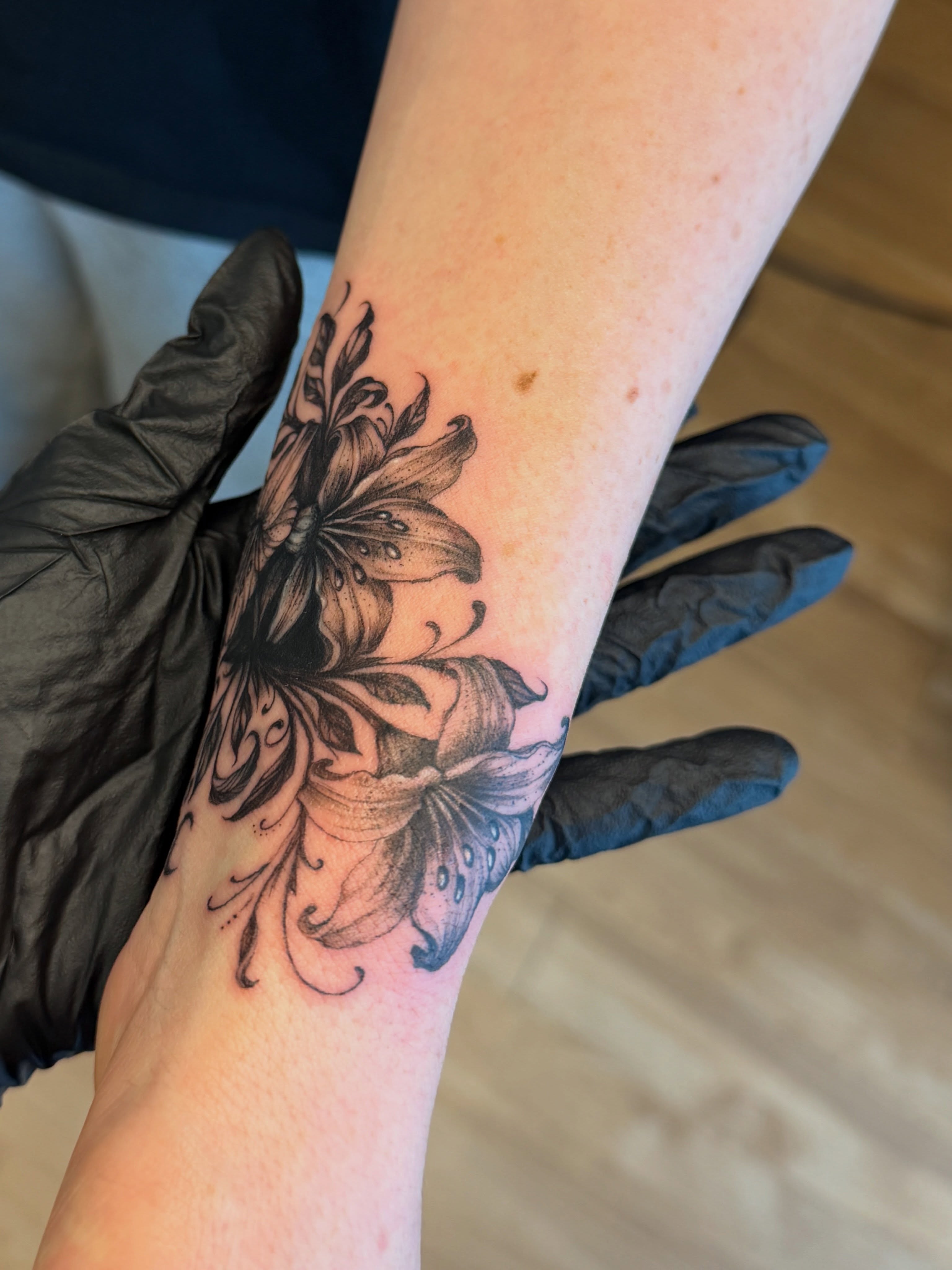 Lily black and grey tattoo on the forearm by Aristova Anastasia