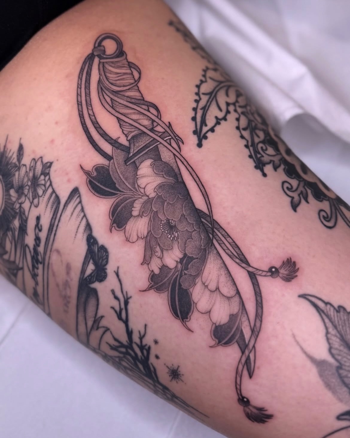 String and floral black and grey tattoo on the forearm by Jena Perry