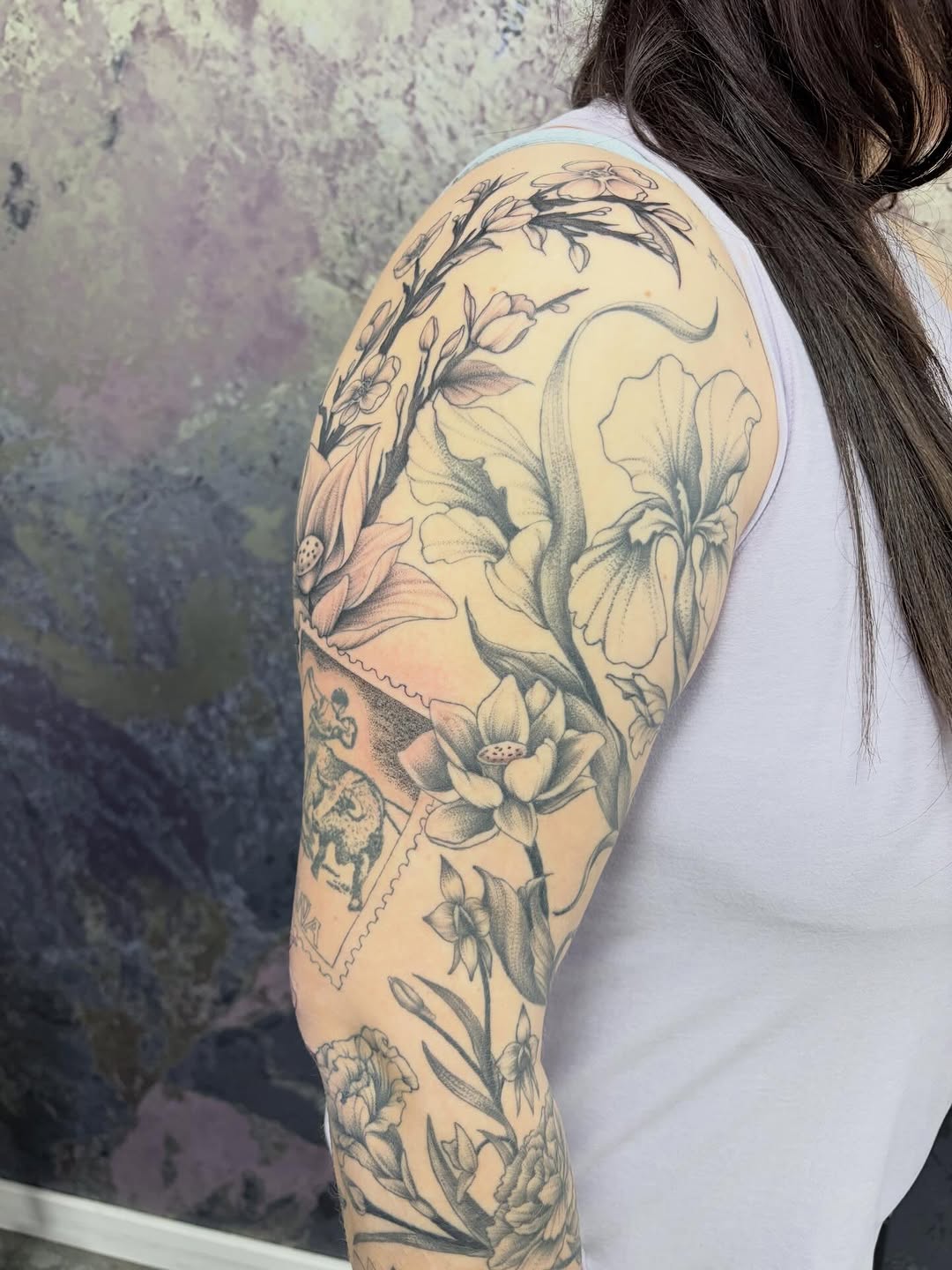 Floral sleeve with postage stamps fine line tattoo on the upper arm by Kenzie Mecham-Cunningham