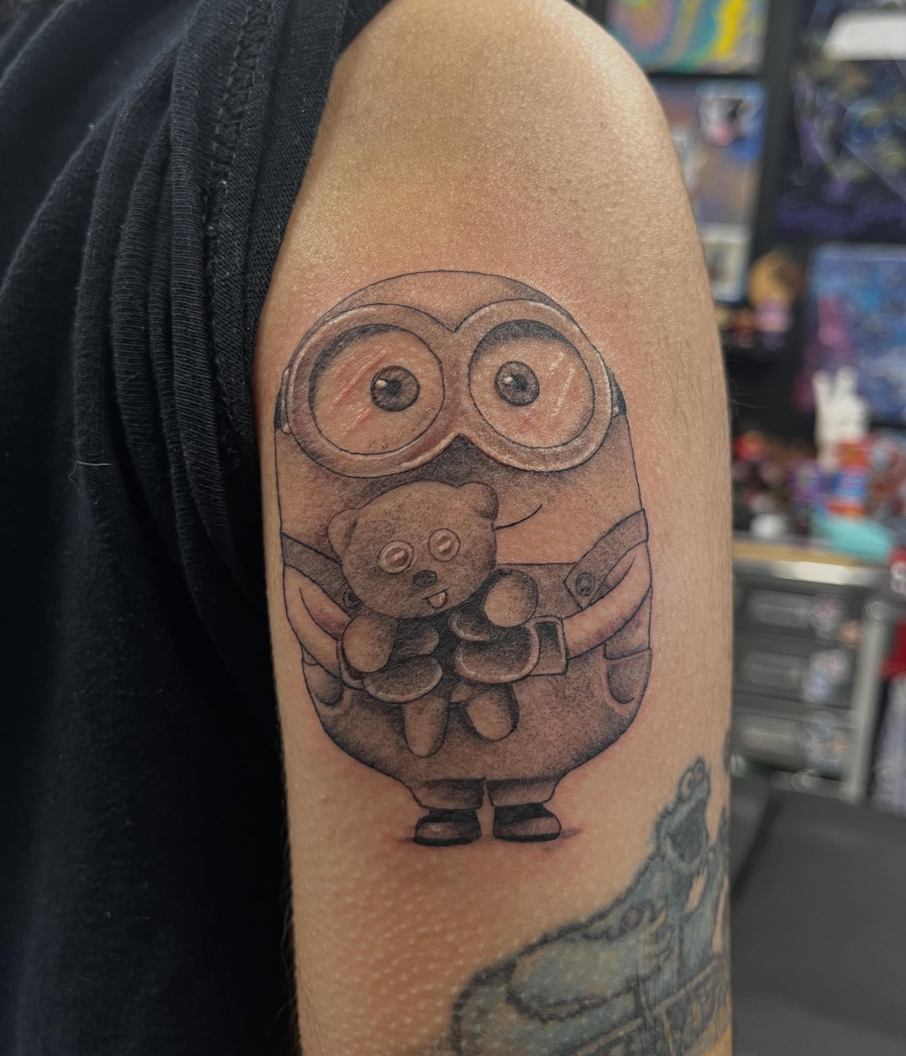 Minion holding teddy bear black and grey tattoo on the forearm by @artinjections667