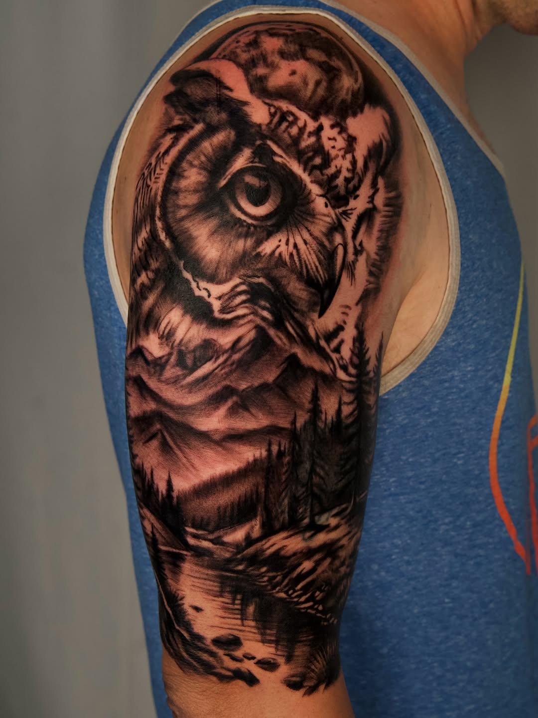Owl and mountain landscape realism tattoo on the upper arm by Nate