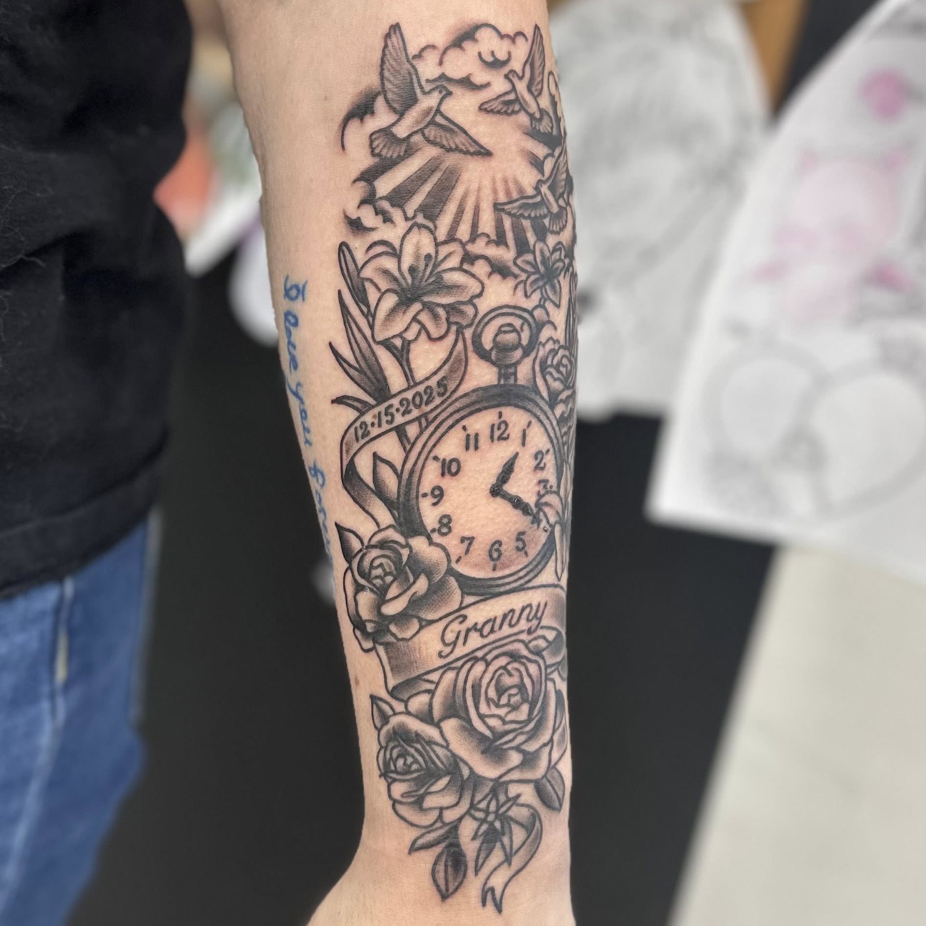 Clock and floral arrangement black and grey tattoo on the forearm by Jon Anderson