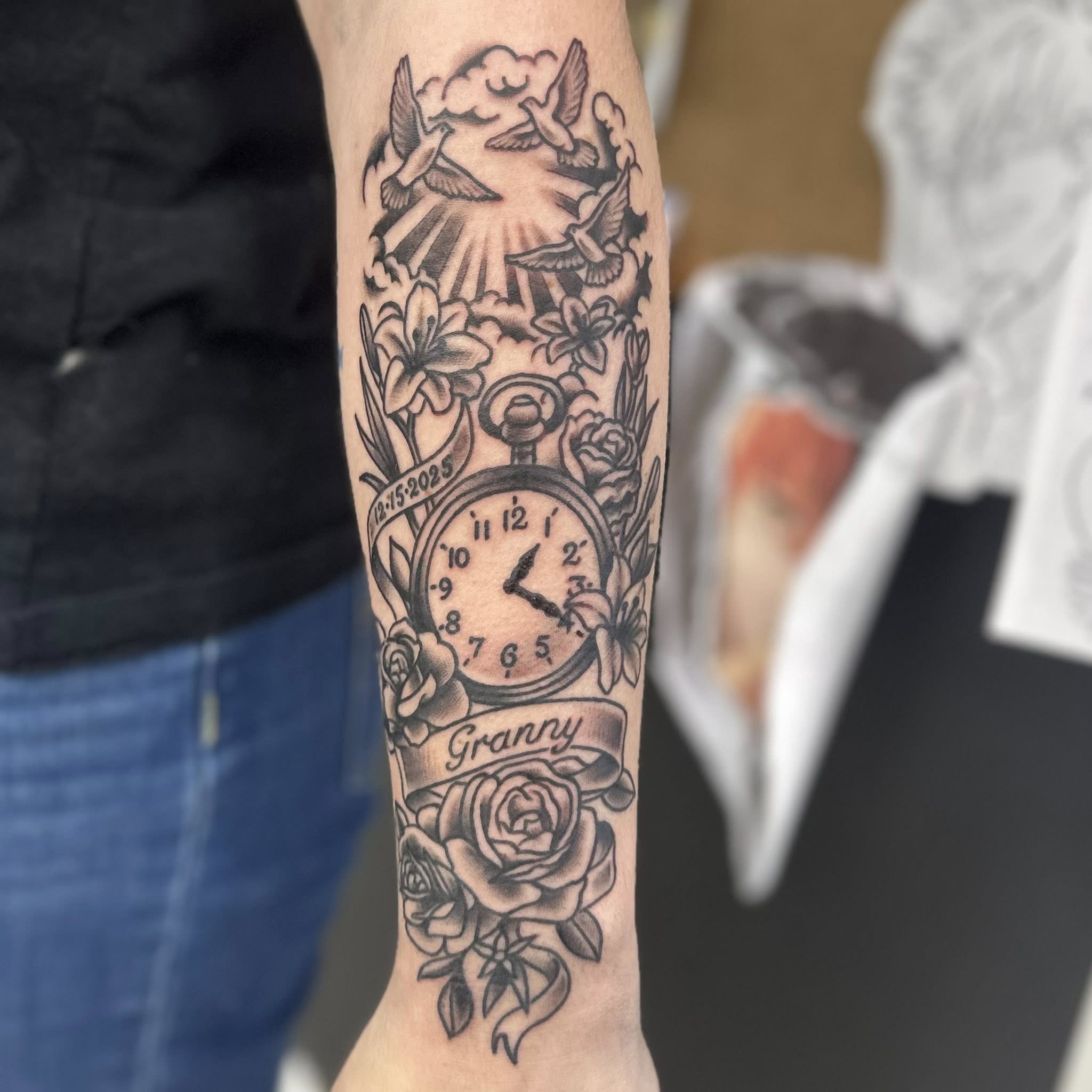 Clock and floral arrangement ornamental tattoo on the forearm by Jon Anderson
