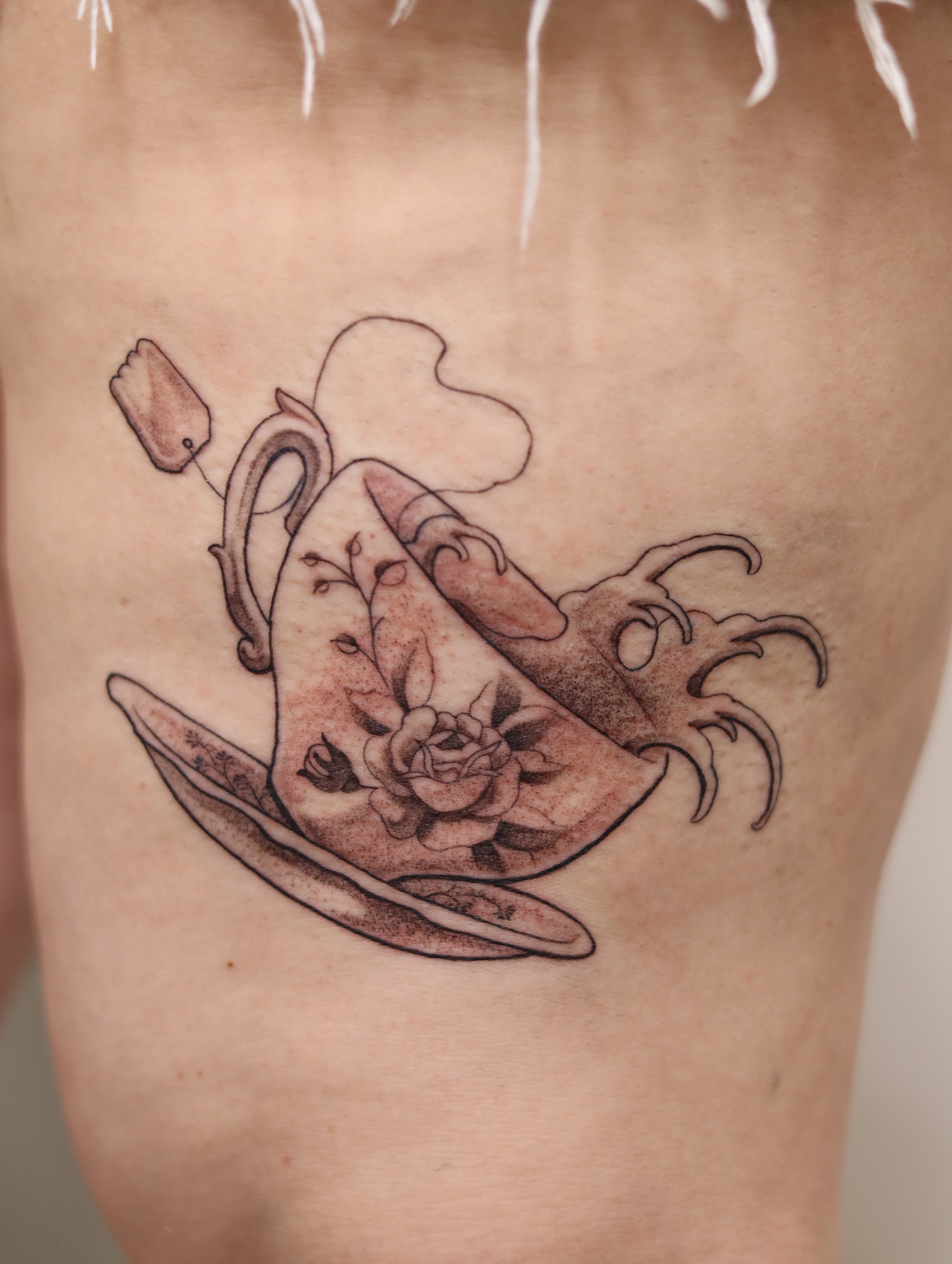 Tea cup and saucer black and grey tattoo on the thigh by Caleb Ortiz