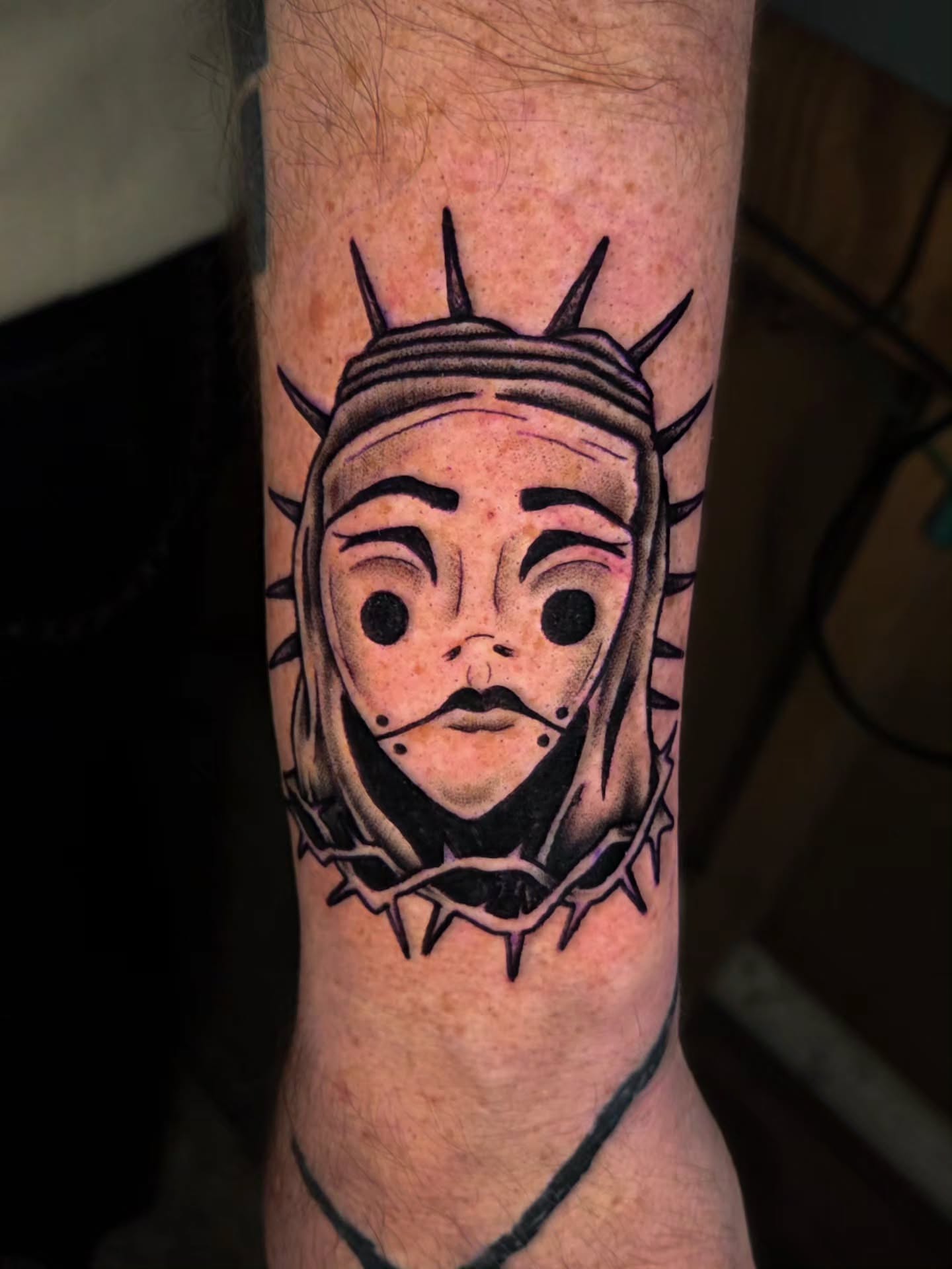 Mask with crown of thorns black and grey tattoo on the forearm by Ian Kiser