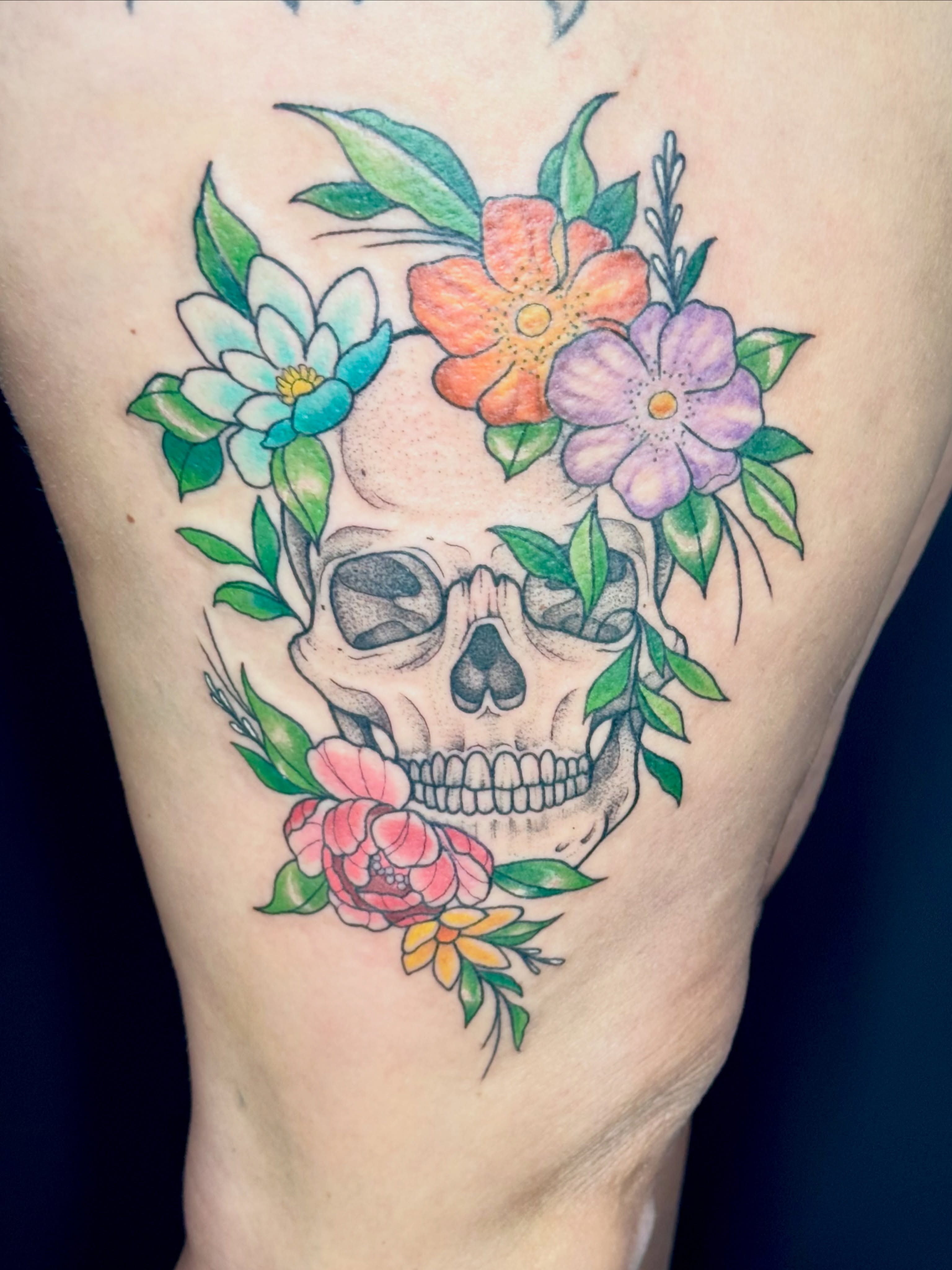Skull with flowers watercolor tattoo on the thigh by Caitlynn Austin