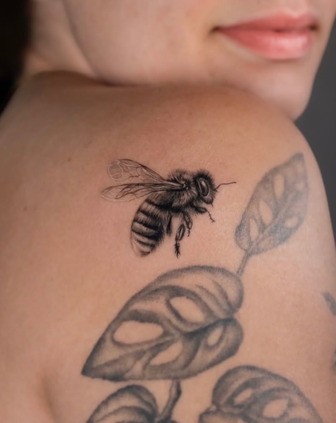 Bee and plant leaves fine line tattoo on the shoulder by Valery Cardona