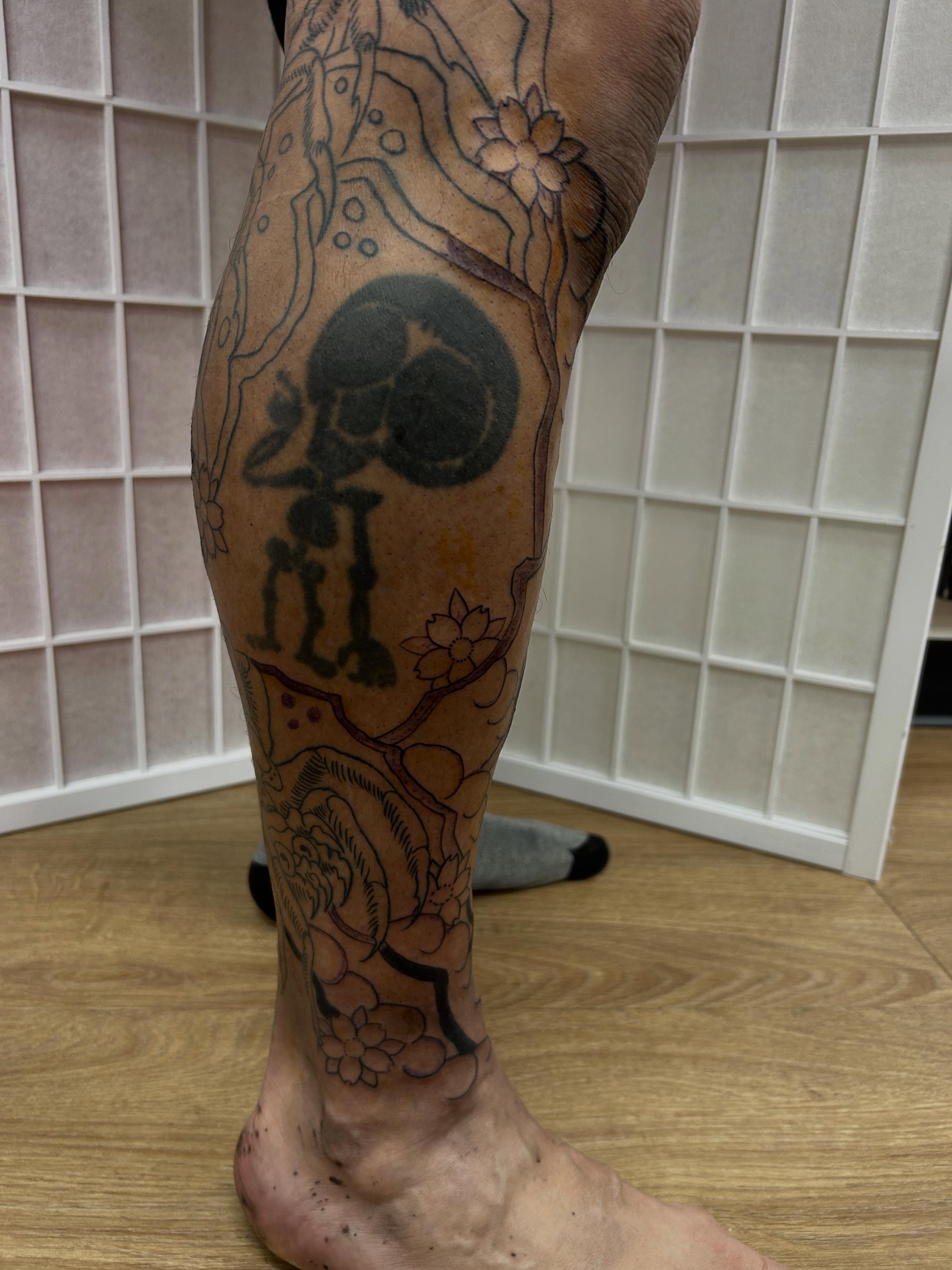 Skull and floral black and grey tattoo on the calf by Stogie Tony