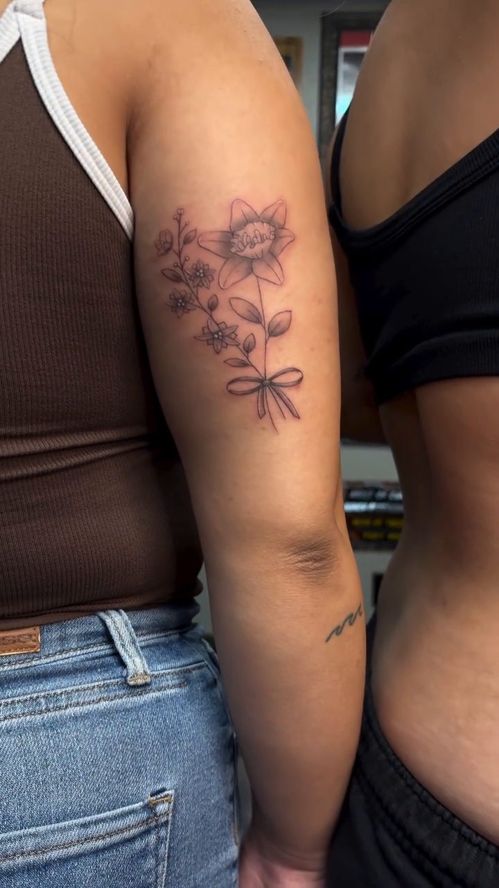 Floral bouquet with bow fine line tattoo on the upper arm by alana khounmeuang