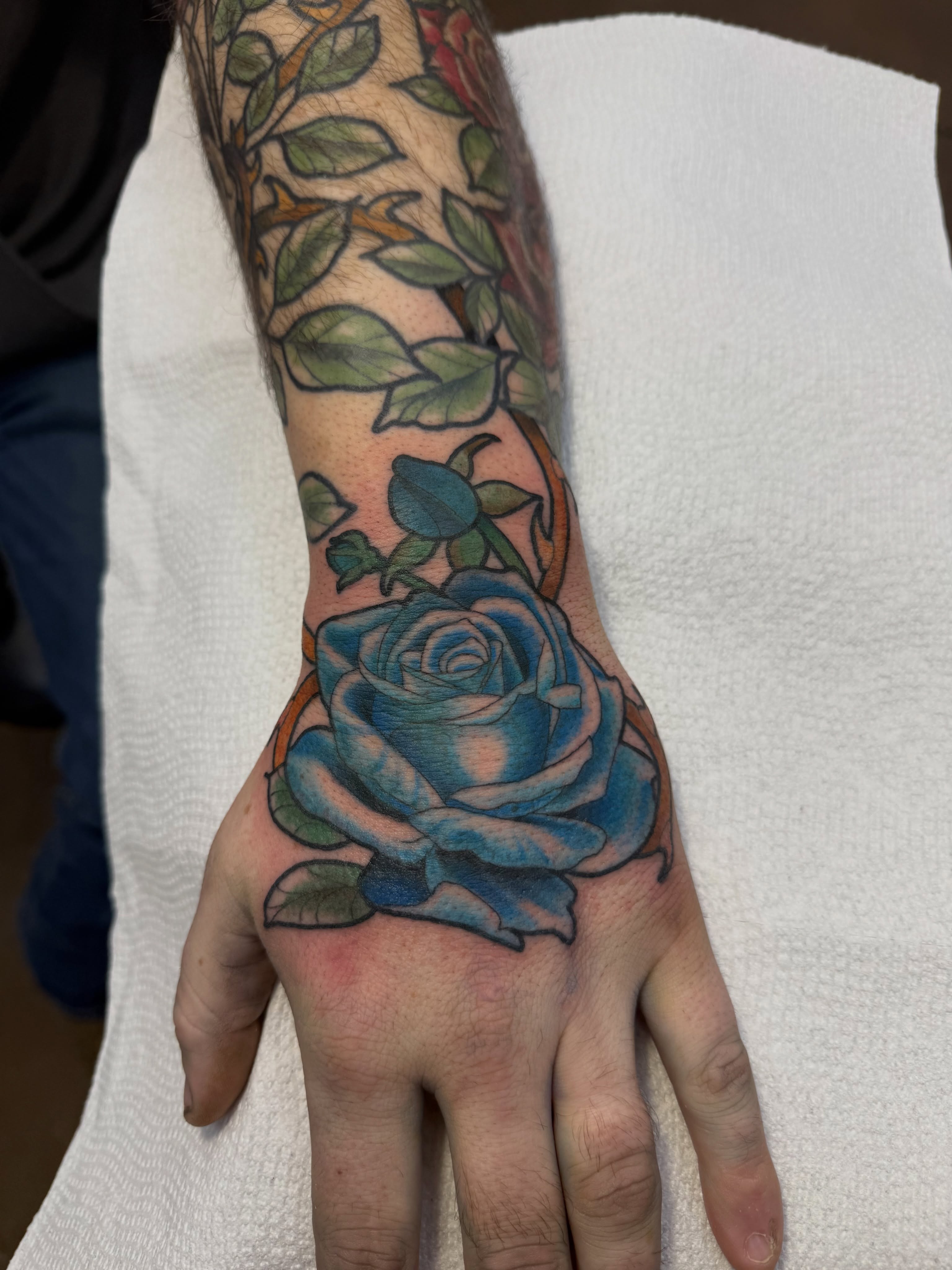 Blue rose realism tattoo on the hand by autumn sky