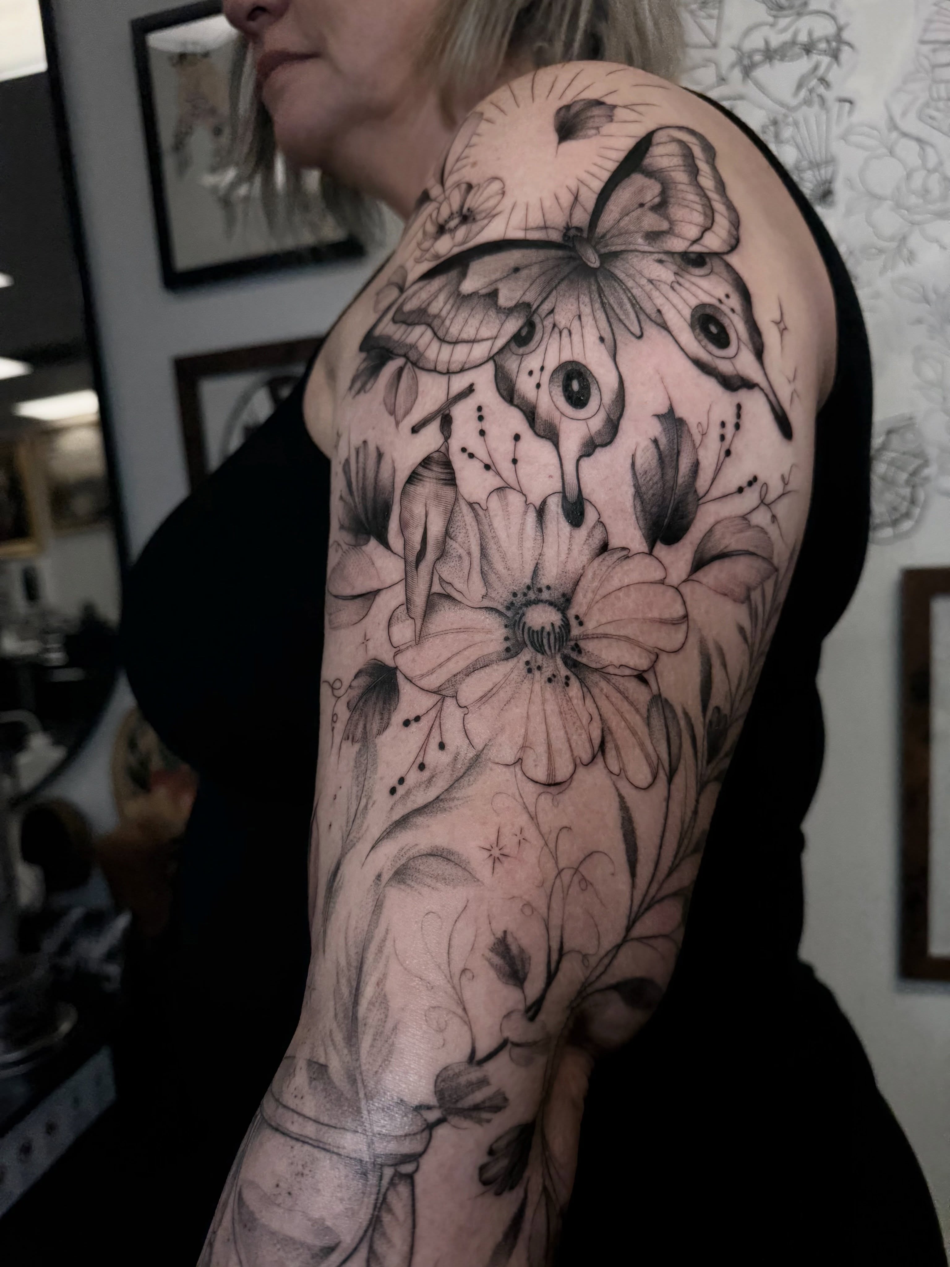 Flowers and butterfly dotwork tattoo on the upper arm by Chloe