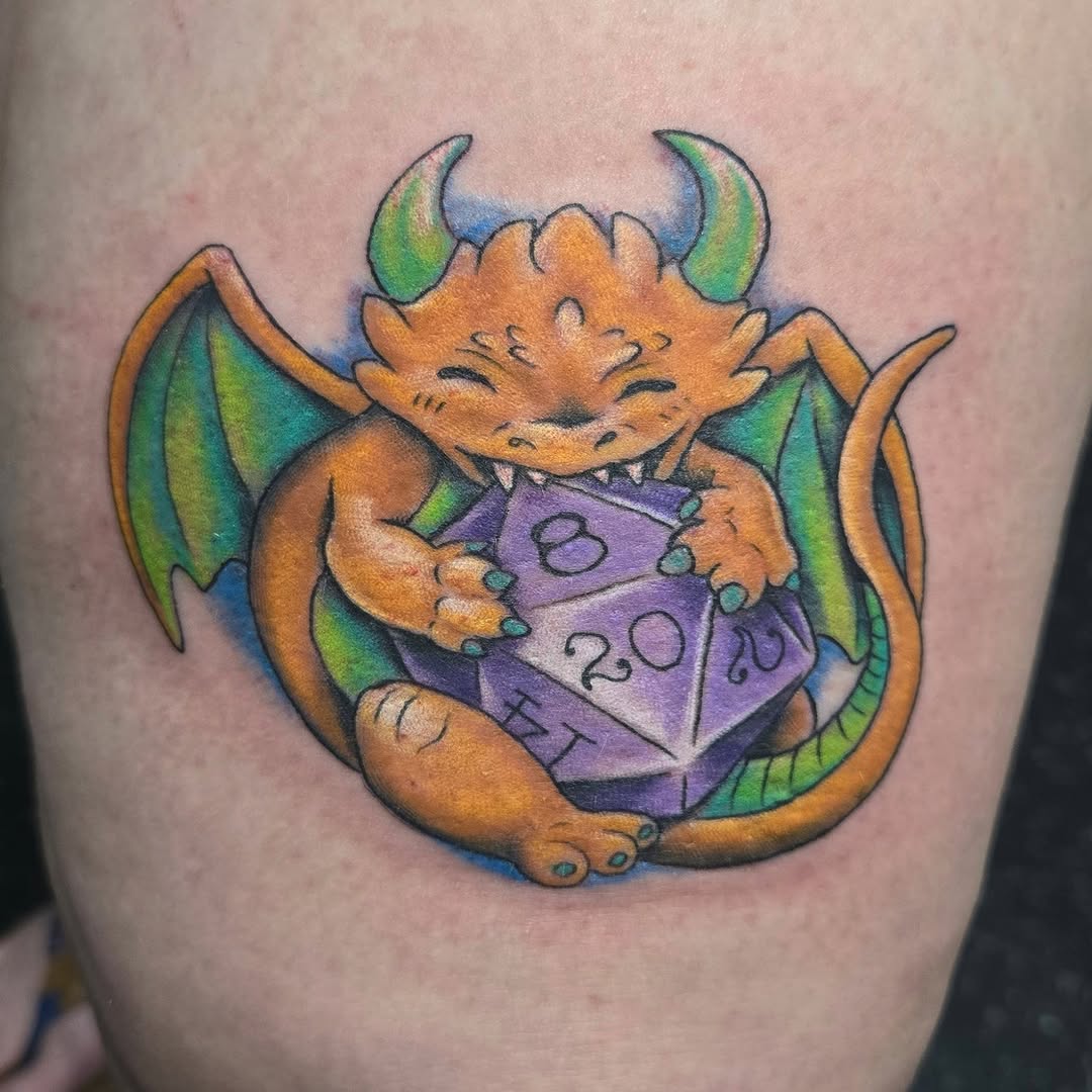 Chibi dragon holding a d20 die new school tattoo on the thigh by ℝ𝕠𝕓𝕚𝕟 𝕄𝕒𝕥𝕫 𝕋𝕒𝕥𝕥𝕠𝕠𝕤