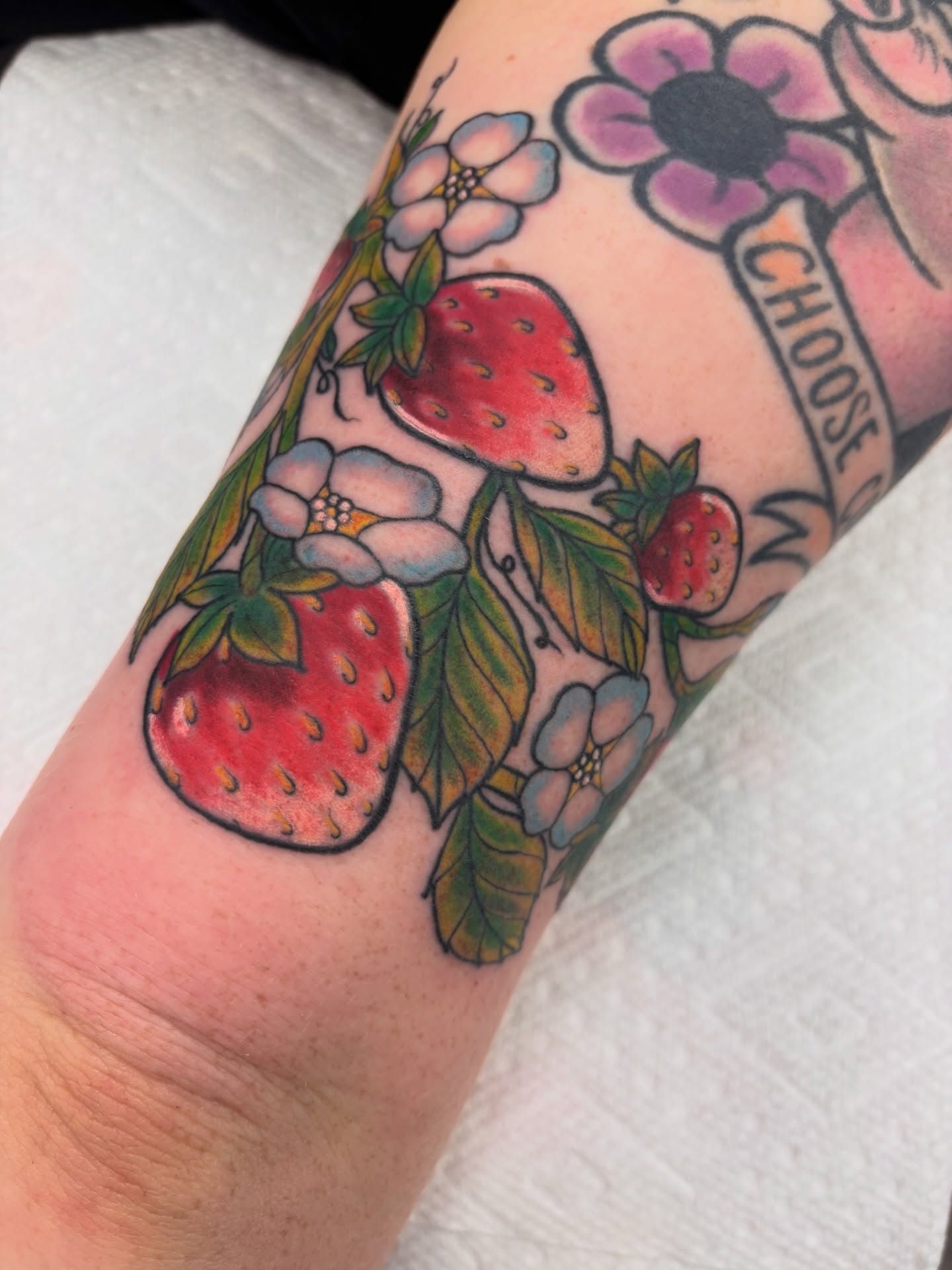 Strawberries and flowers American traditional tattoo on the forearm by Megan