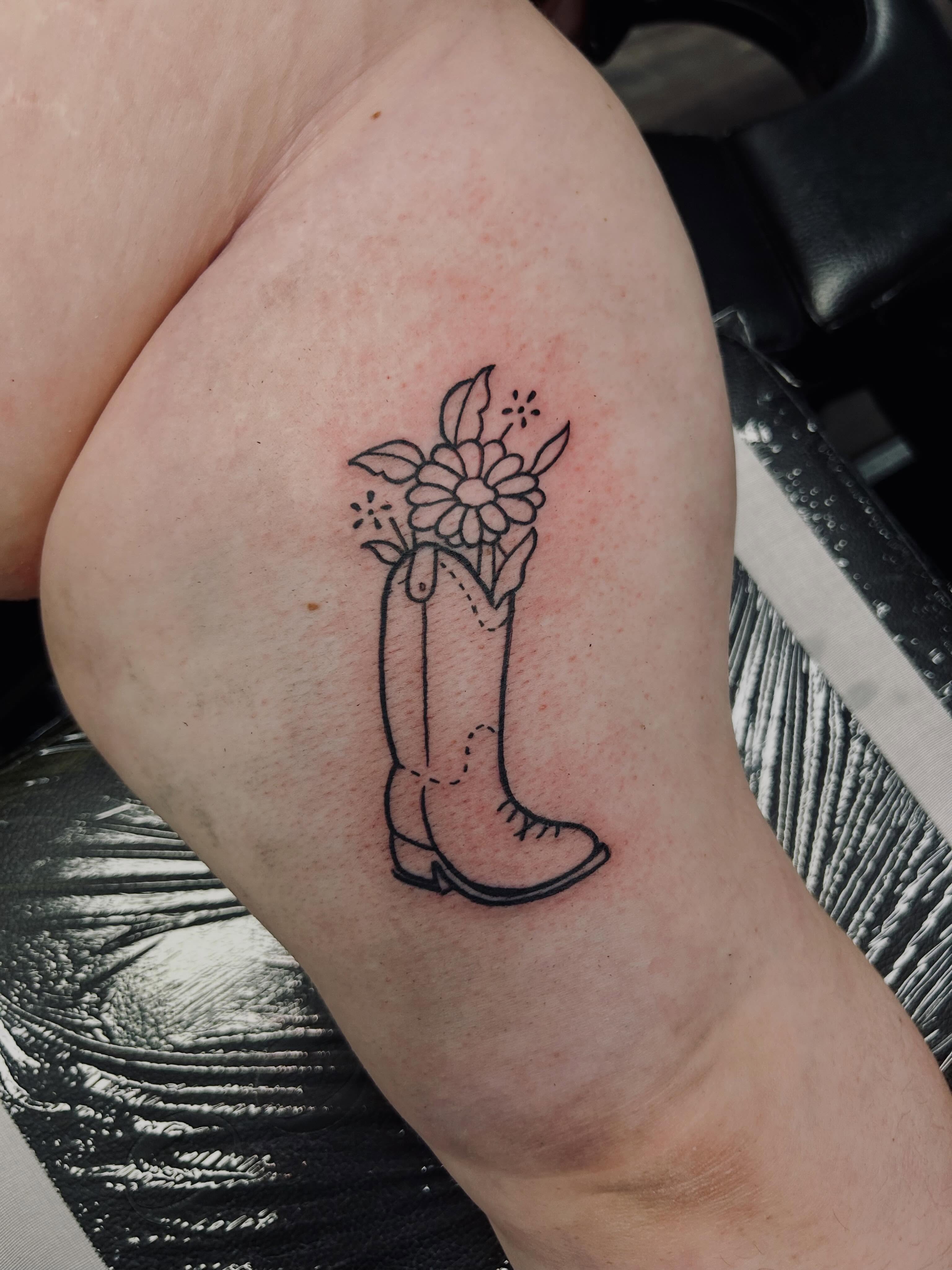 Cowboy boot with flowers black and grey tattoo on the thigh by Bjorn Bjornstad, Dubuque, Iowa