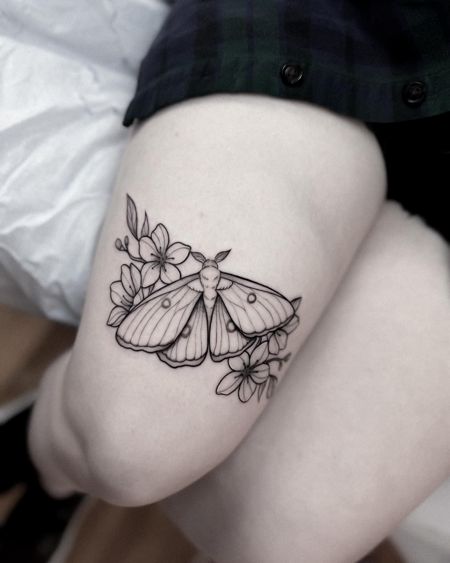 Moth and flowers black and grey tattoo on the thigh by Whimsical Tattoos
