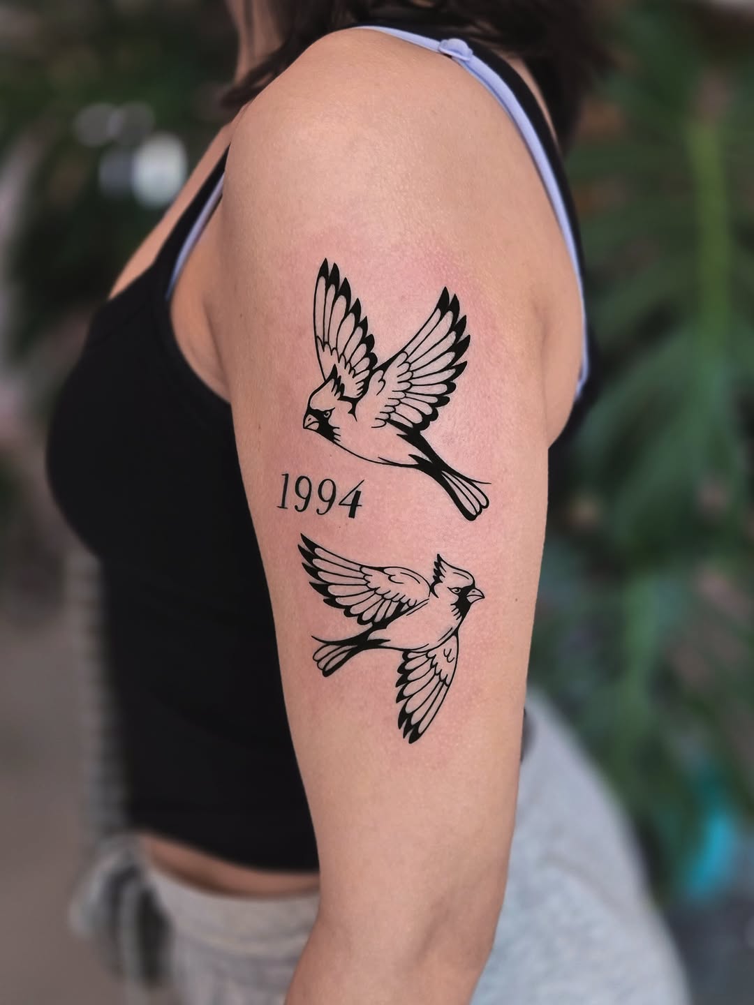 Two birds and year fine line tattoo on the upper arm by Kirstie Lew Tattoo