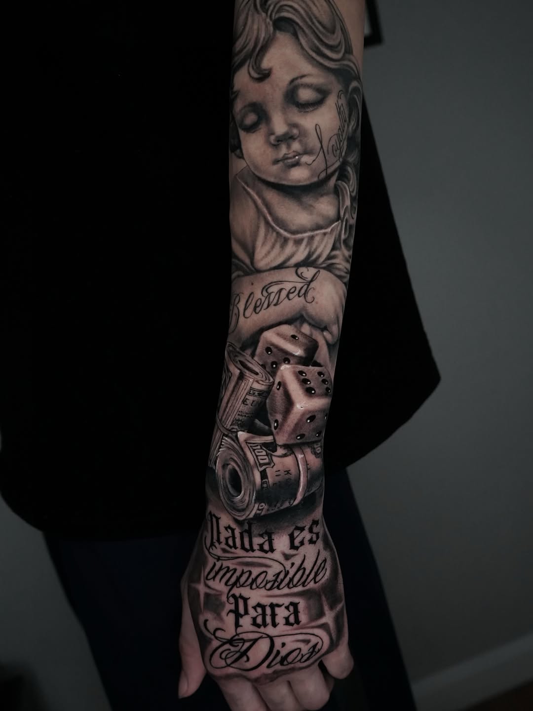 Cherub, dice, money, and script Chicano tattoo on the forearm by Carlos Trujillo
