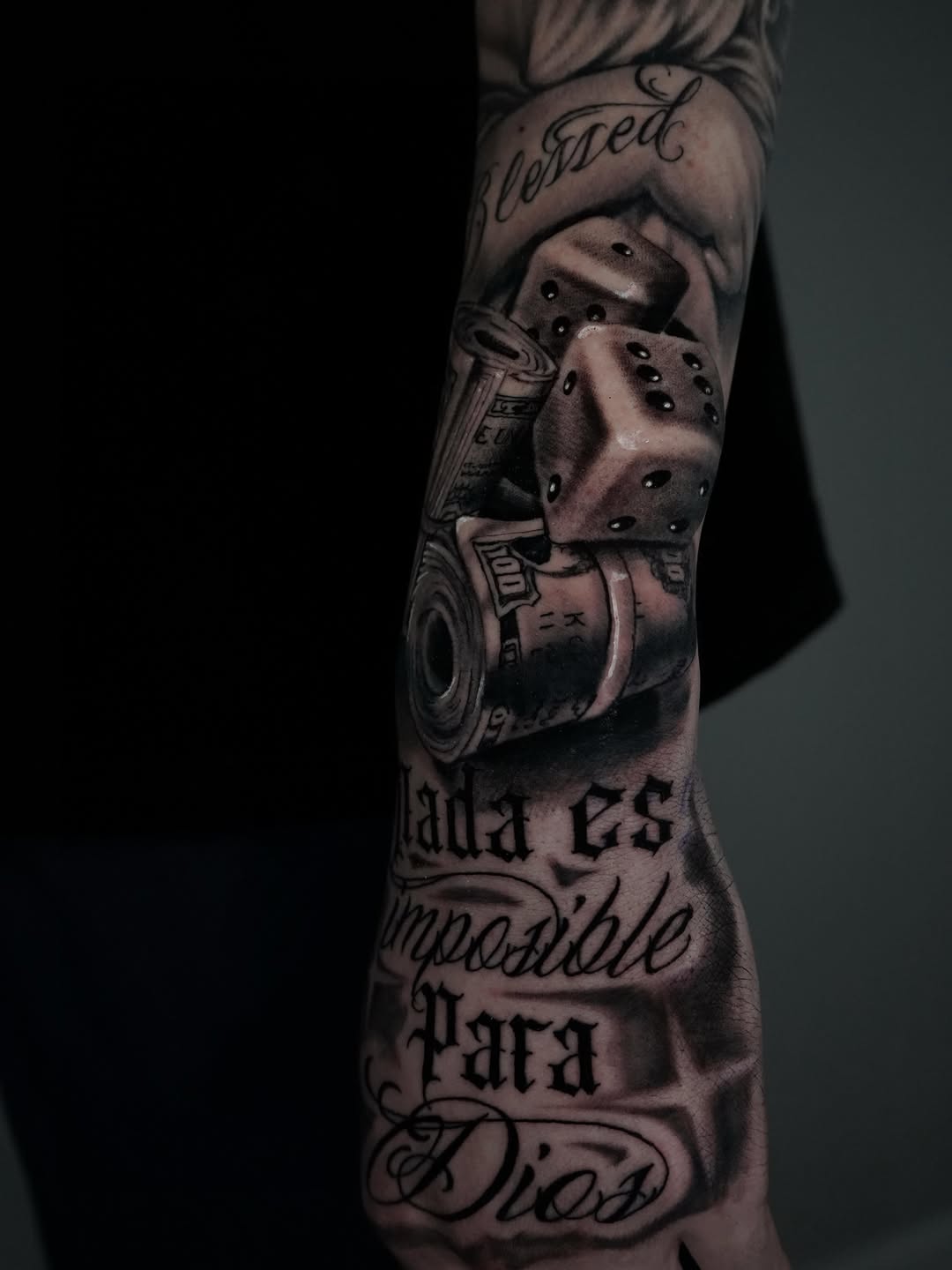 Dice, money, and script Chicano tattoo on the forearm by Carlos Trujillo