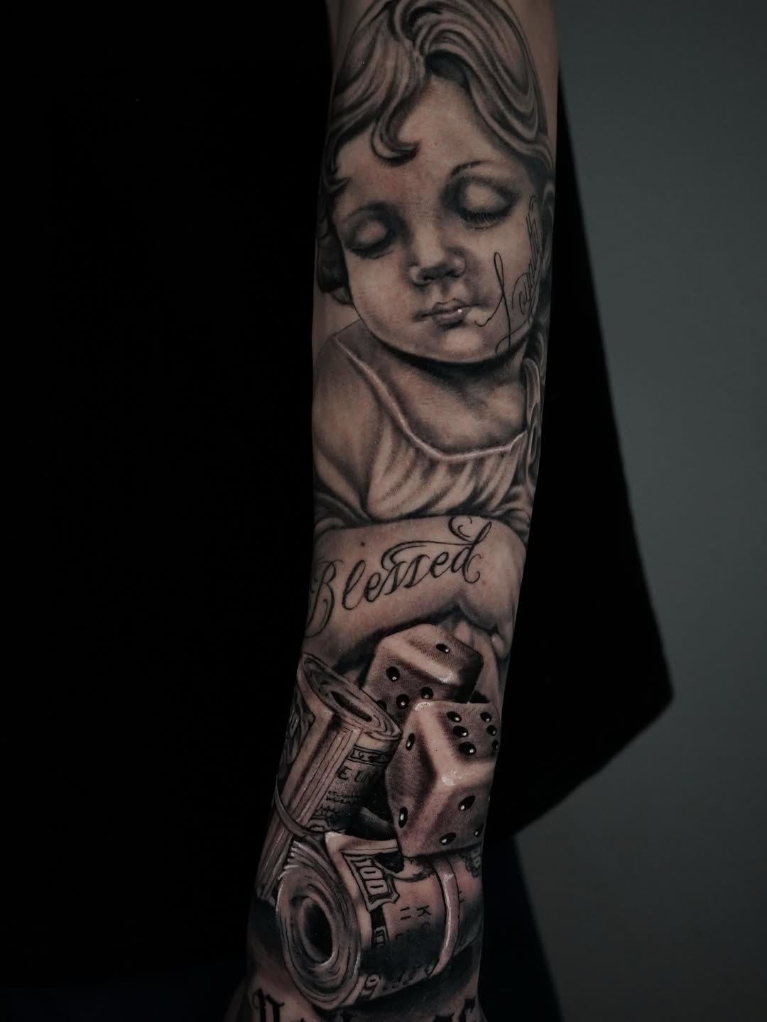 Cherub, dice, and money realism tattoo on the forearm by Carlos Trujillo
