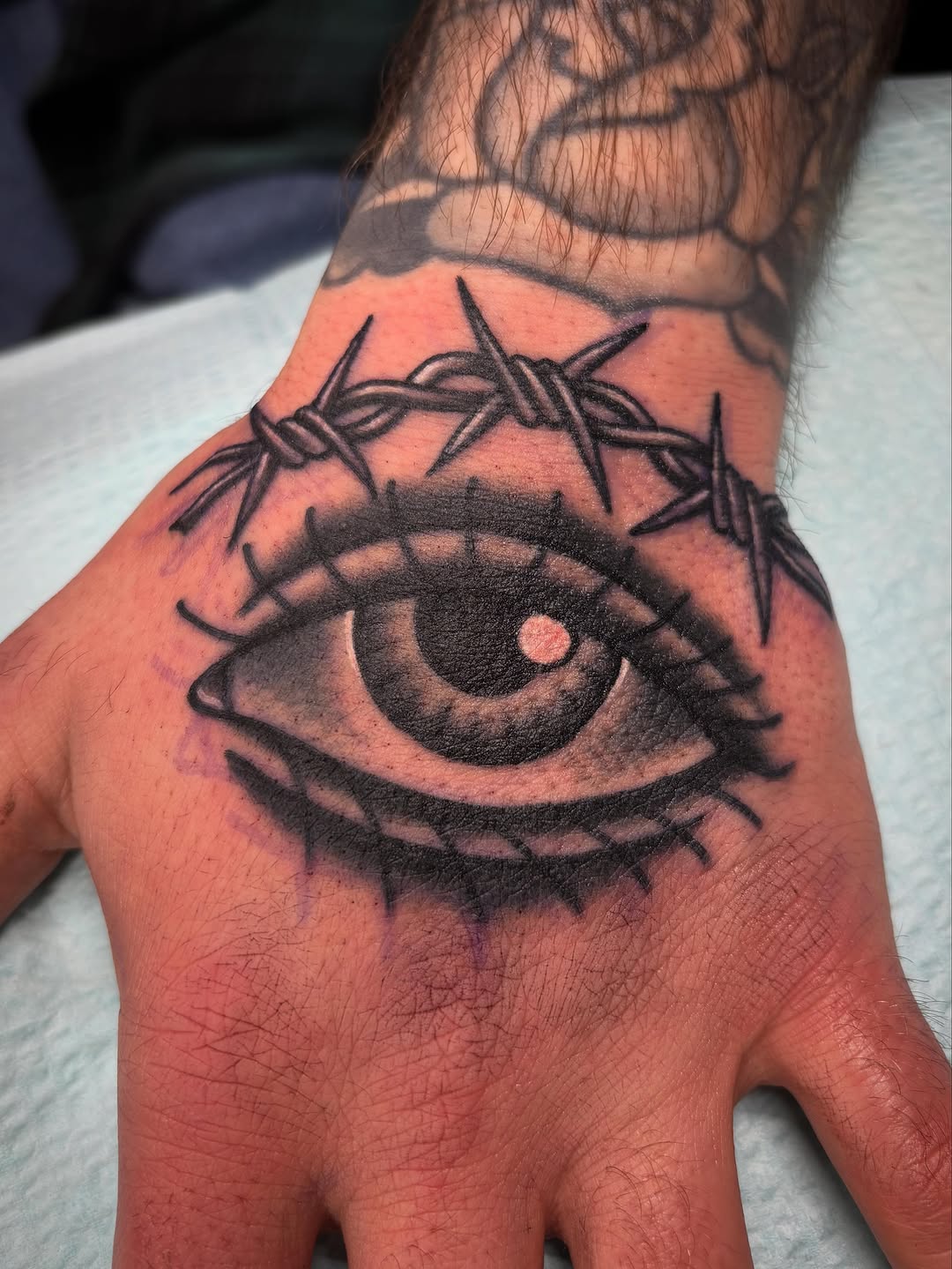 Eye and barbed wire dark art tattoo on the hand by Tom Wenzell