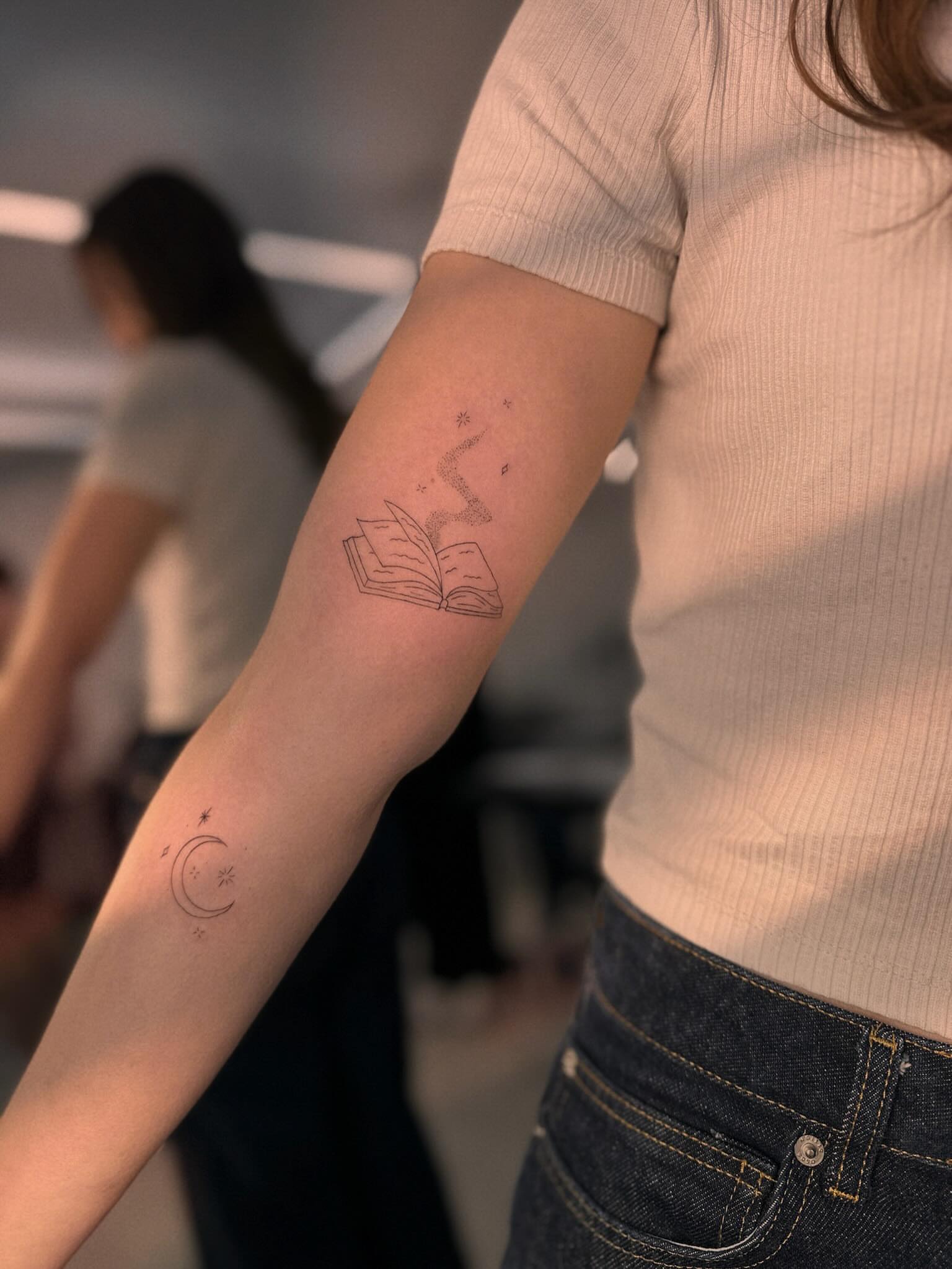 Book and crescent moon fine line tattoo on the forearm by Ellie