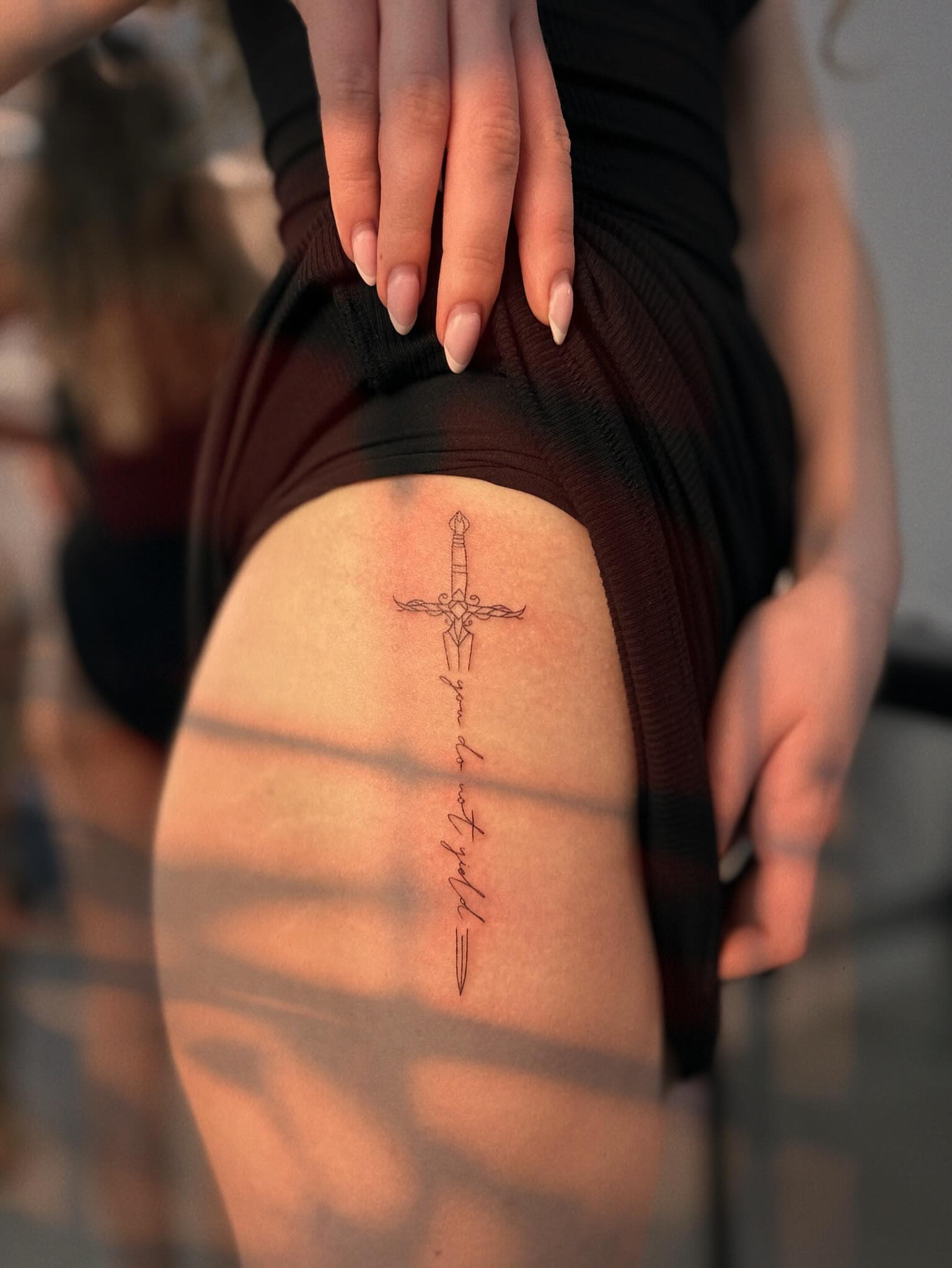 Sword and cross fine line tattoo on the thigh by Ellie