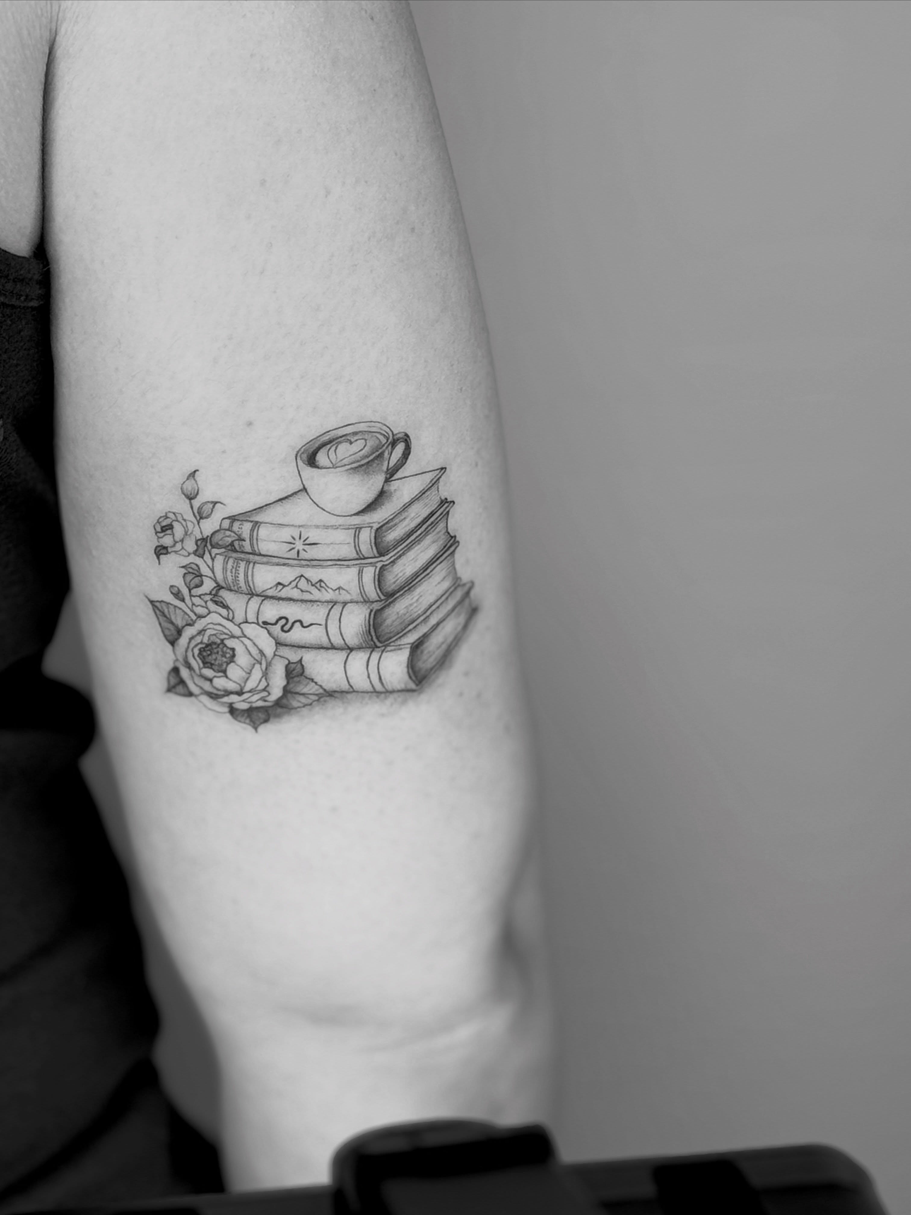 Stack of books and coffee cup realism tattoo on the forearm by Ashley Limon