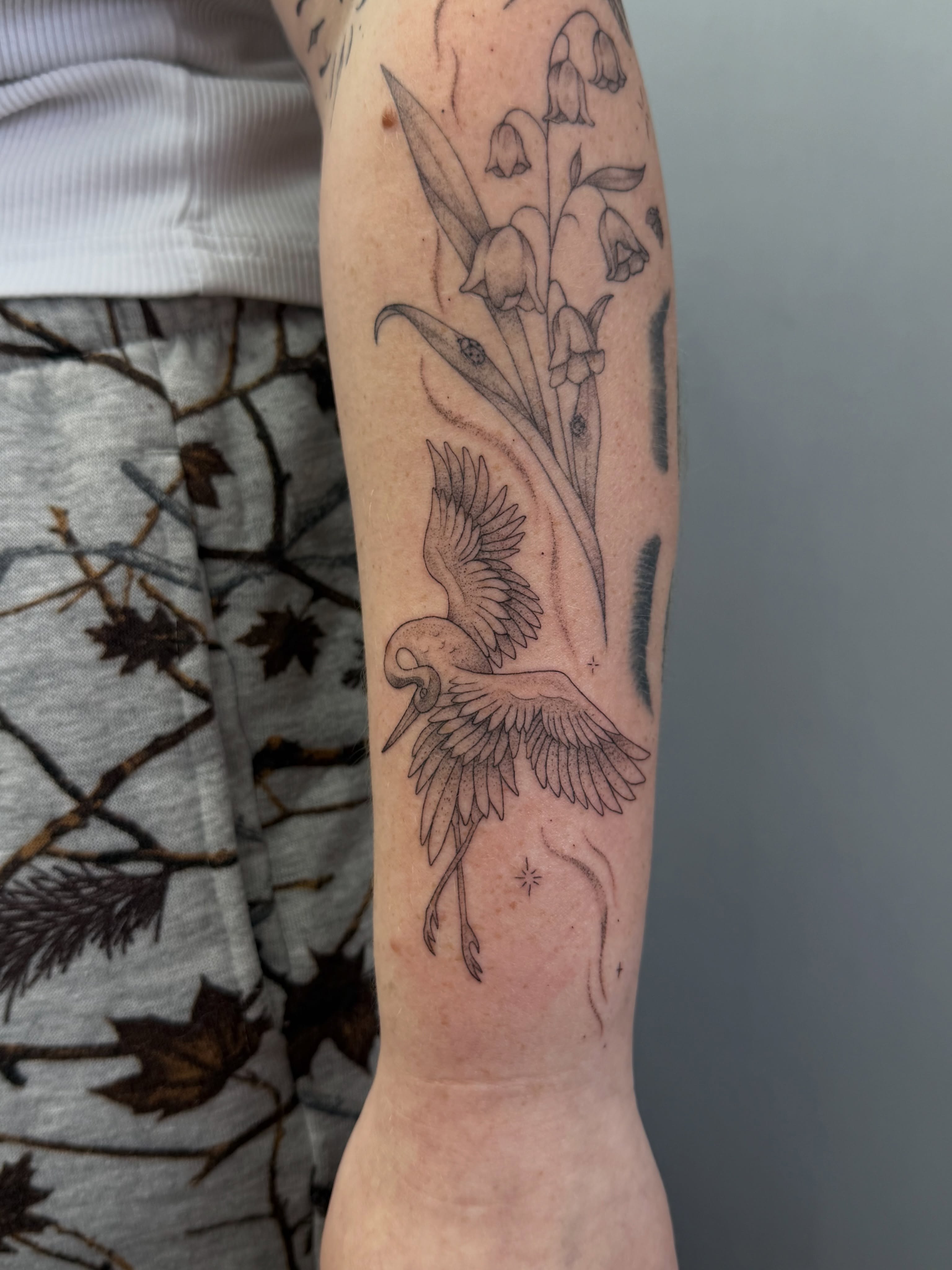 Heron and lily of the valley black and grey tattoo on the forearm by Henesee Parfitt