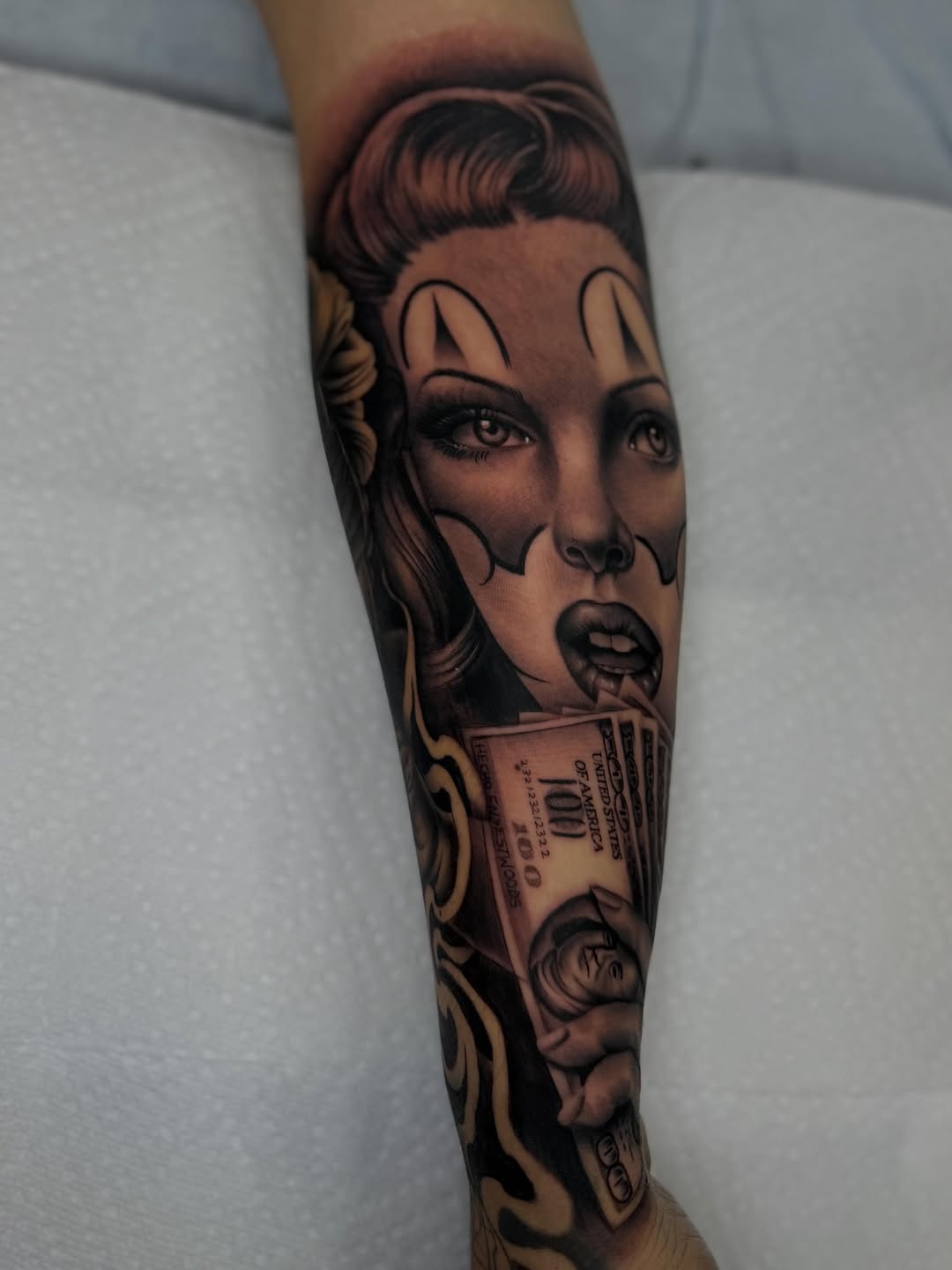 Woman with clown makeup and money Chicano tattoo on the forearm by LOS