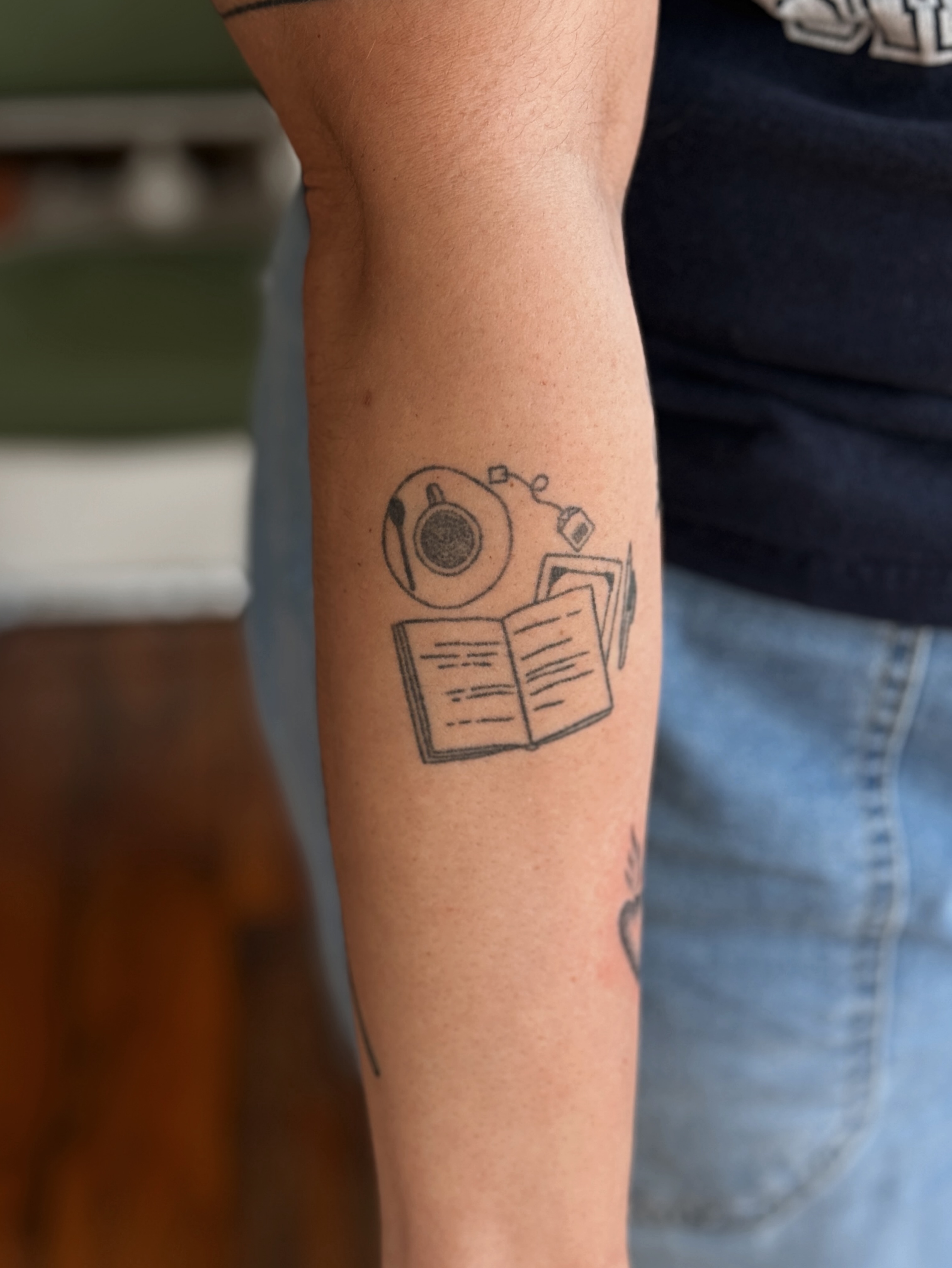 Book and coffee cup black and grey tattoo on the forearm by Grace Wise - Handpoke Tattoos