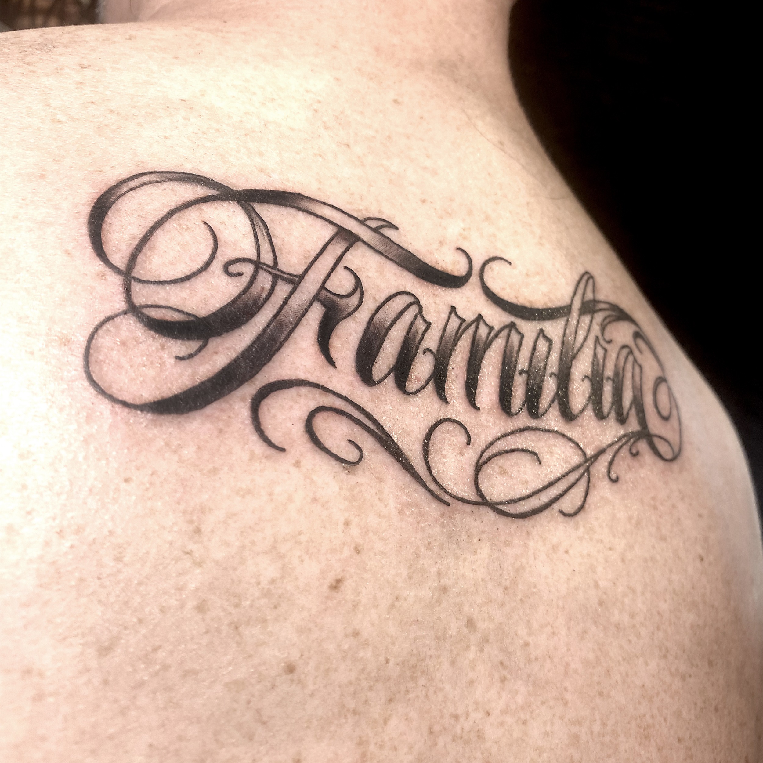 Familia lettering script tattoo on the shoulder by R o s e