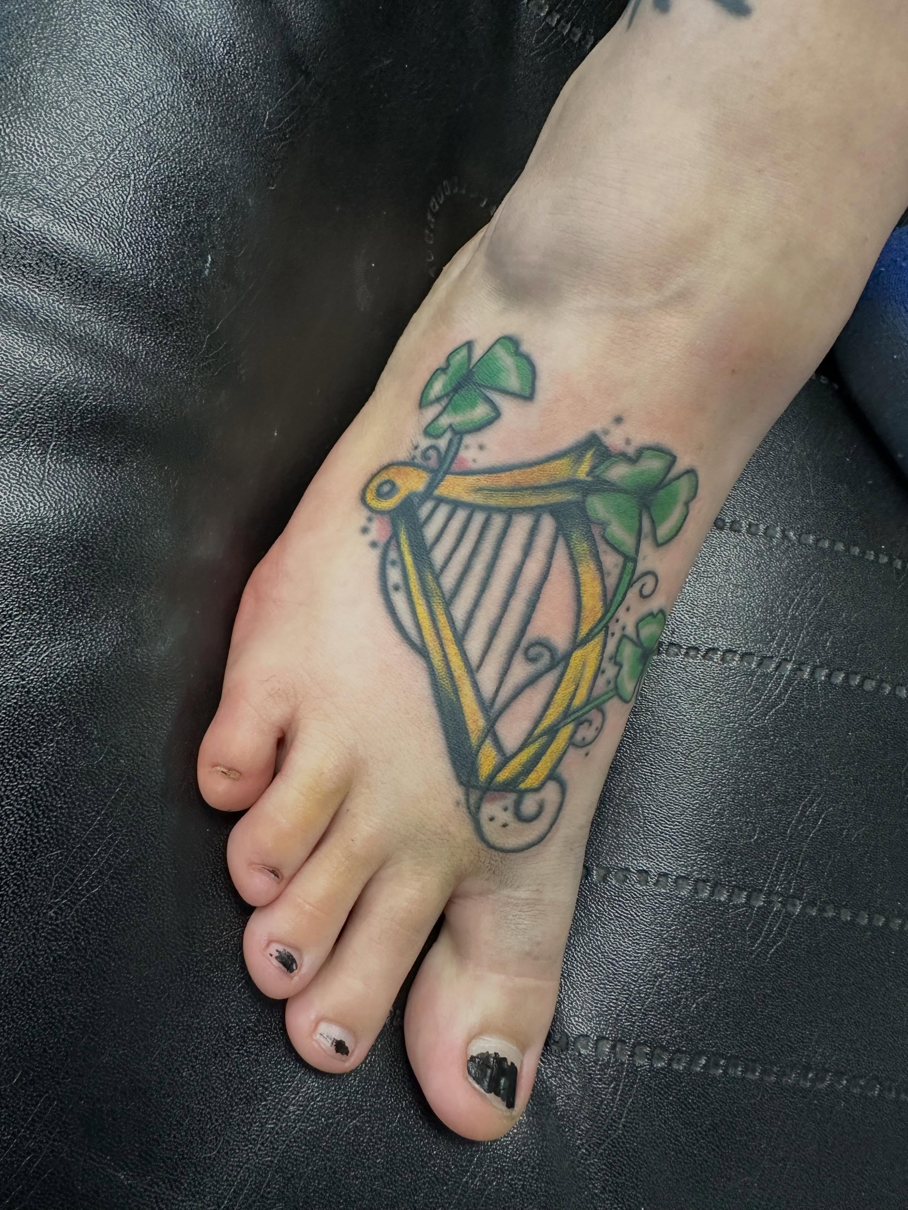 Irish harp and shamrocks American traditional tattoo on the foot by Vincent Merys