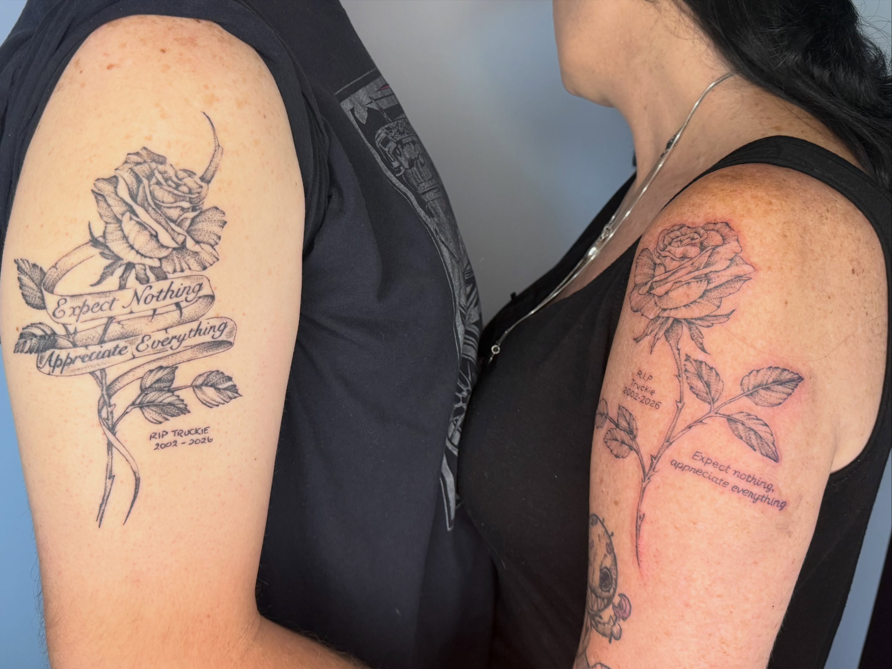 Rose with banner black and grey tattoo on the upper arm by Brandie