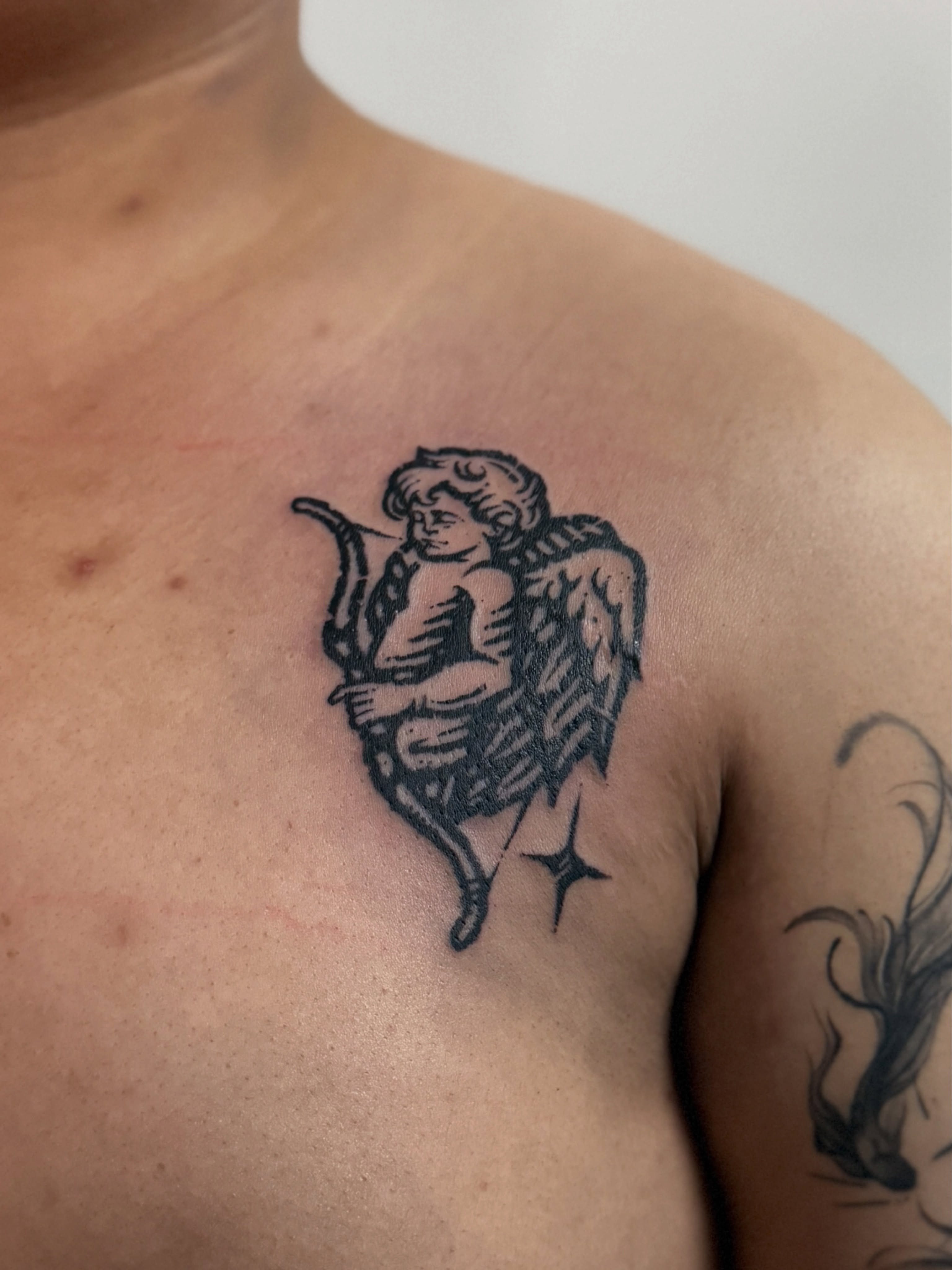 Cherub with bow black and grey tattoo on the chest by ✥台南木兆刺青✥𝕸𝖔𝕸𝖔𝕿𝖆𝖙𝖙𝖔𝖔
