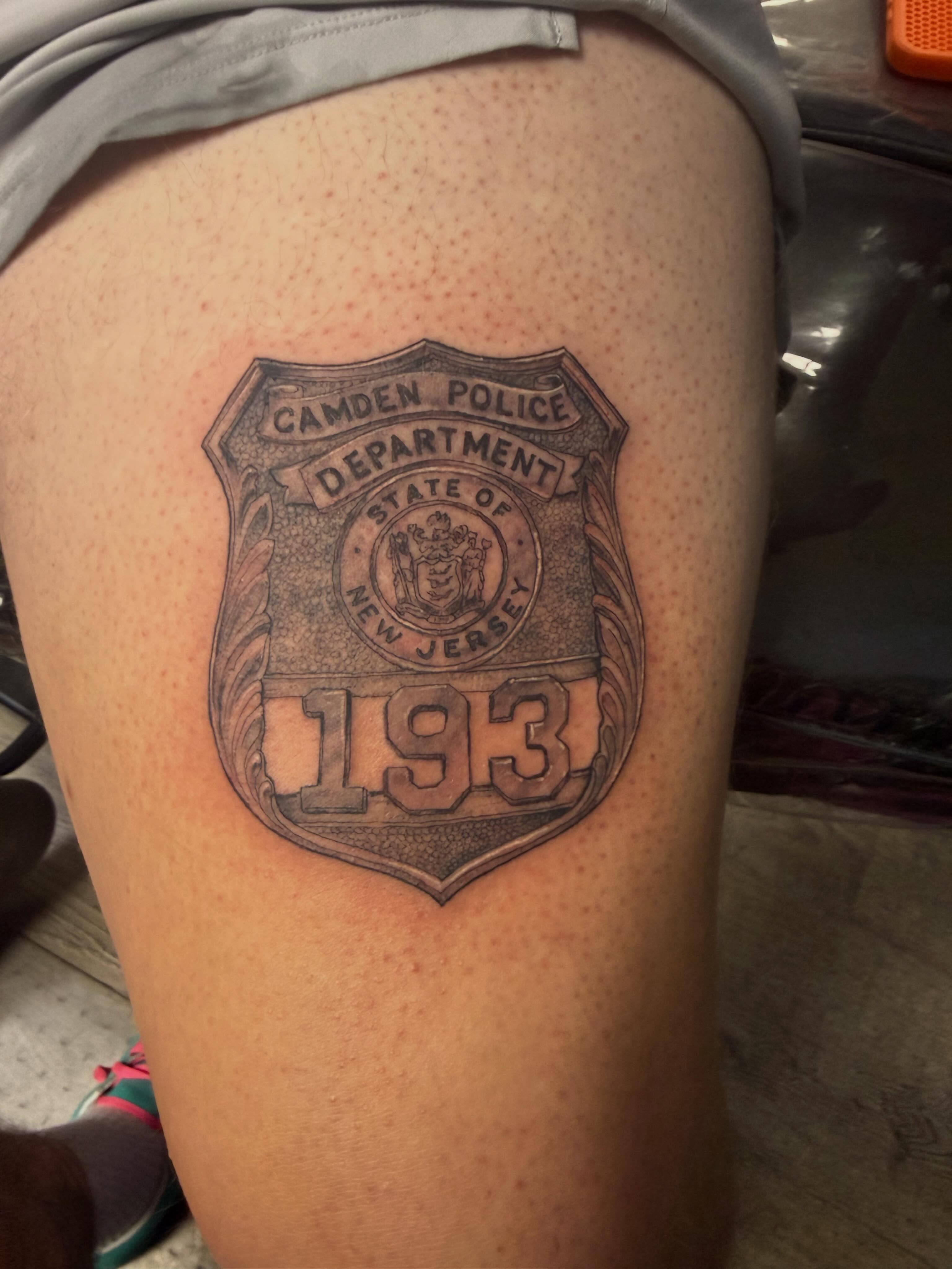 Camden police badge black and grey tattoo on the thigh by Matthew Humphrey, Pawcatuck, Connecticut