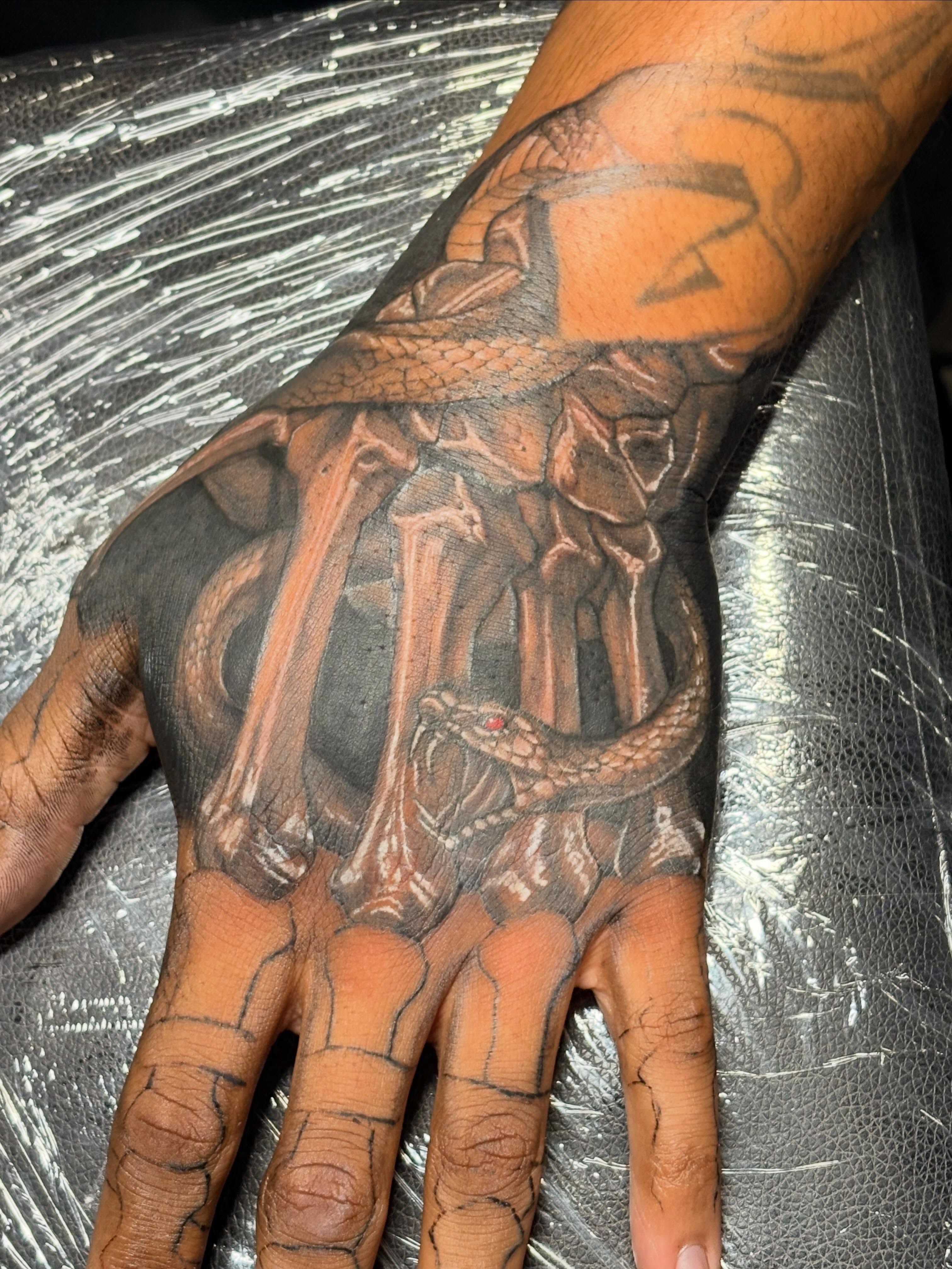 Skeleton hand with snake realism tattoo on the hand by Slade Nowicki