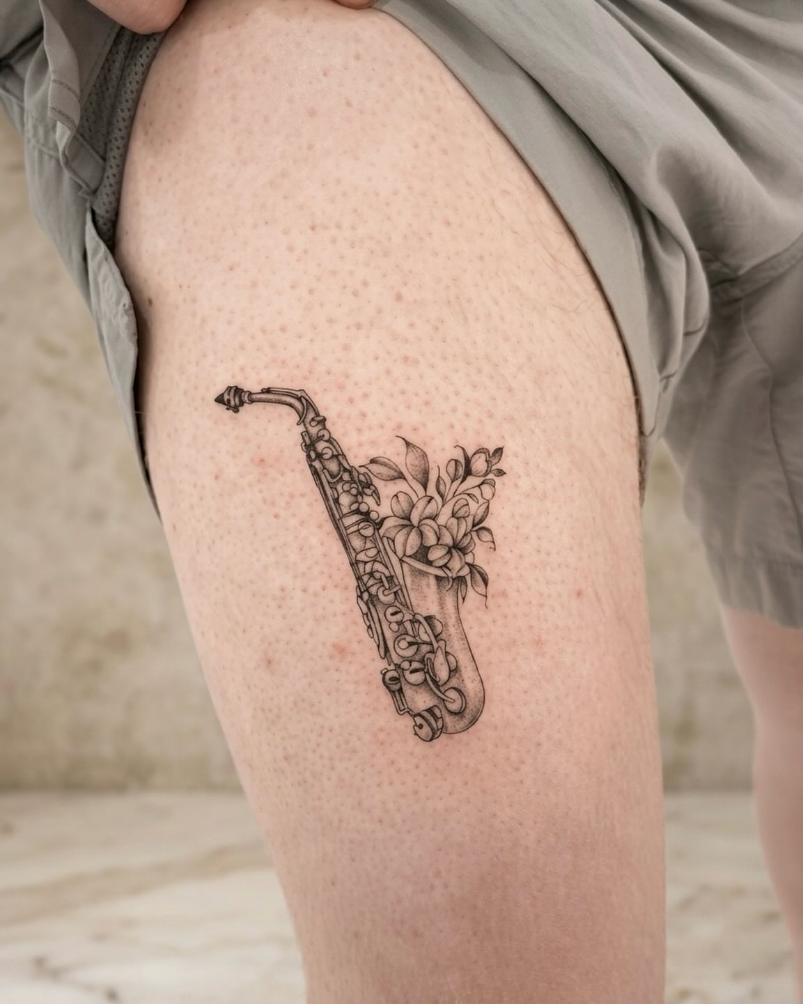 Saxophone and flowers black and grey tattoo on the thigh by Raytattooist