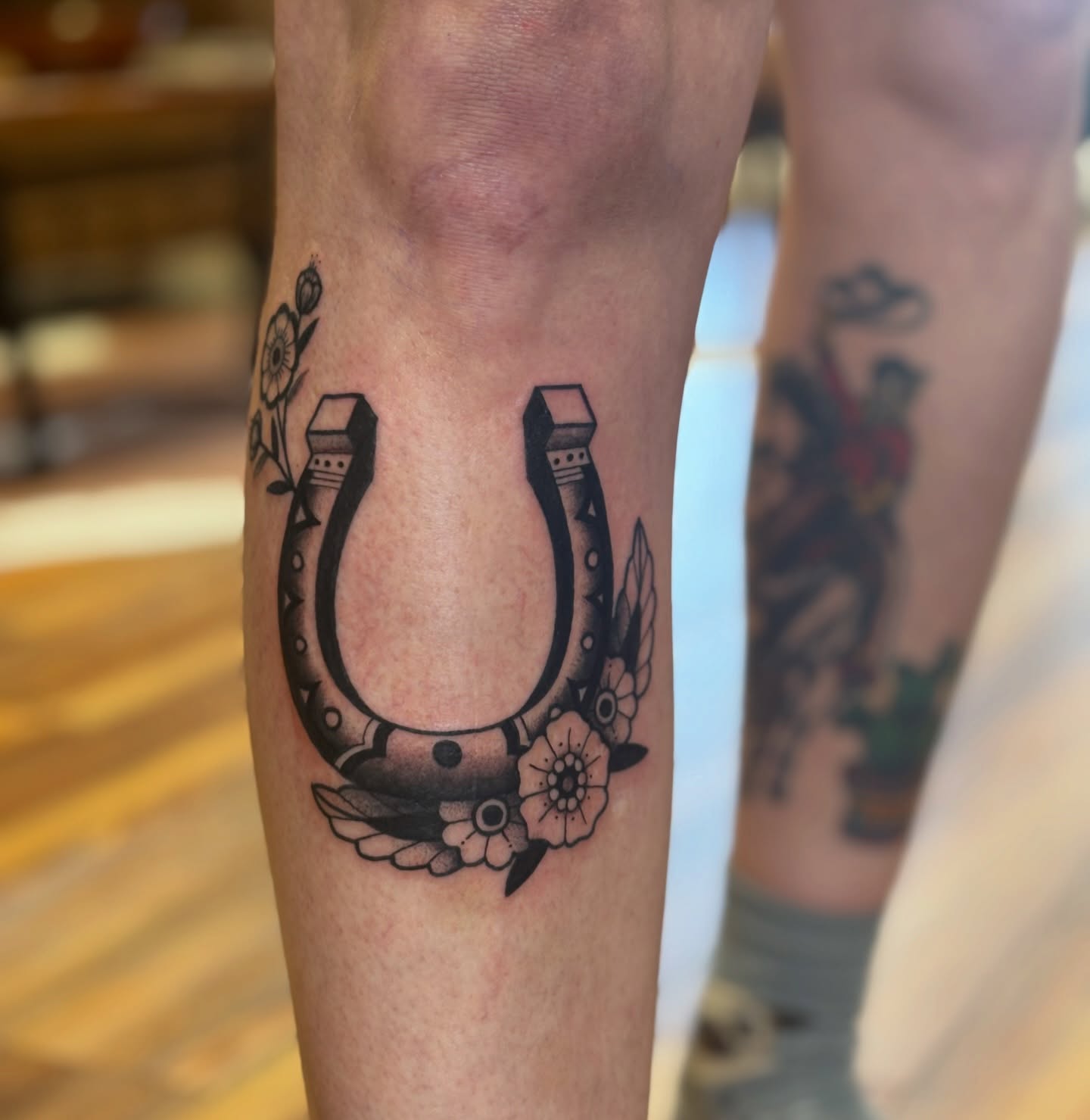 Horseshoe with flowers black and grey tattoo on the forearm by MJ Saunders